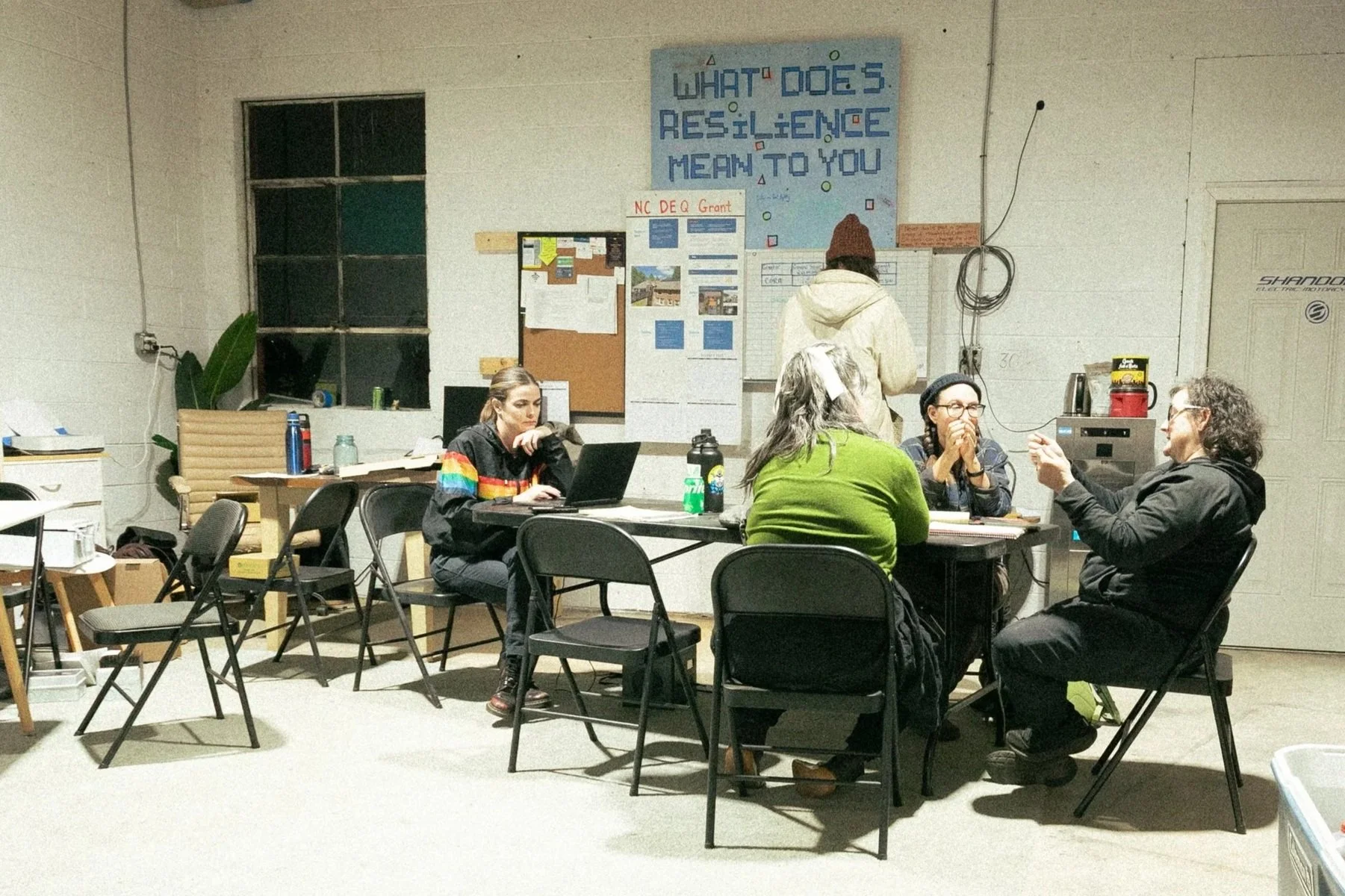A group of people sitting and working at a table in a warehouse.