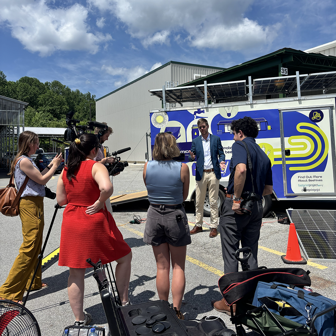 A group of press gather around Will Heergaard at the launch of the Beehive Microgrid at Manna Food Bank.