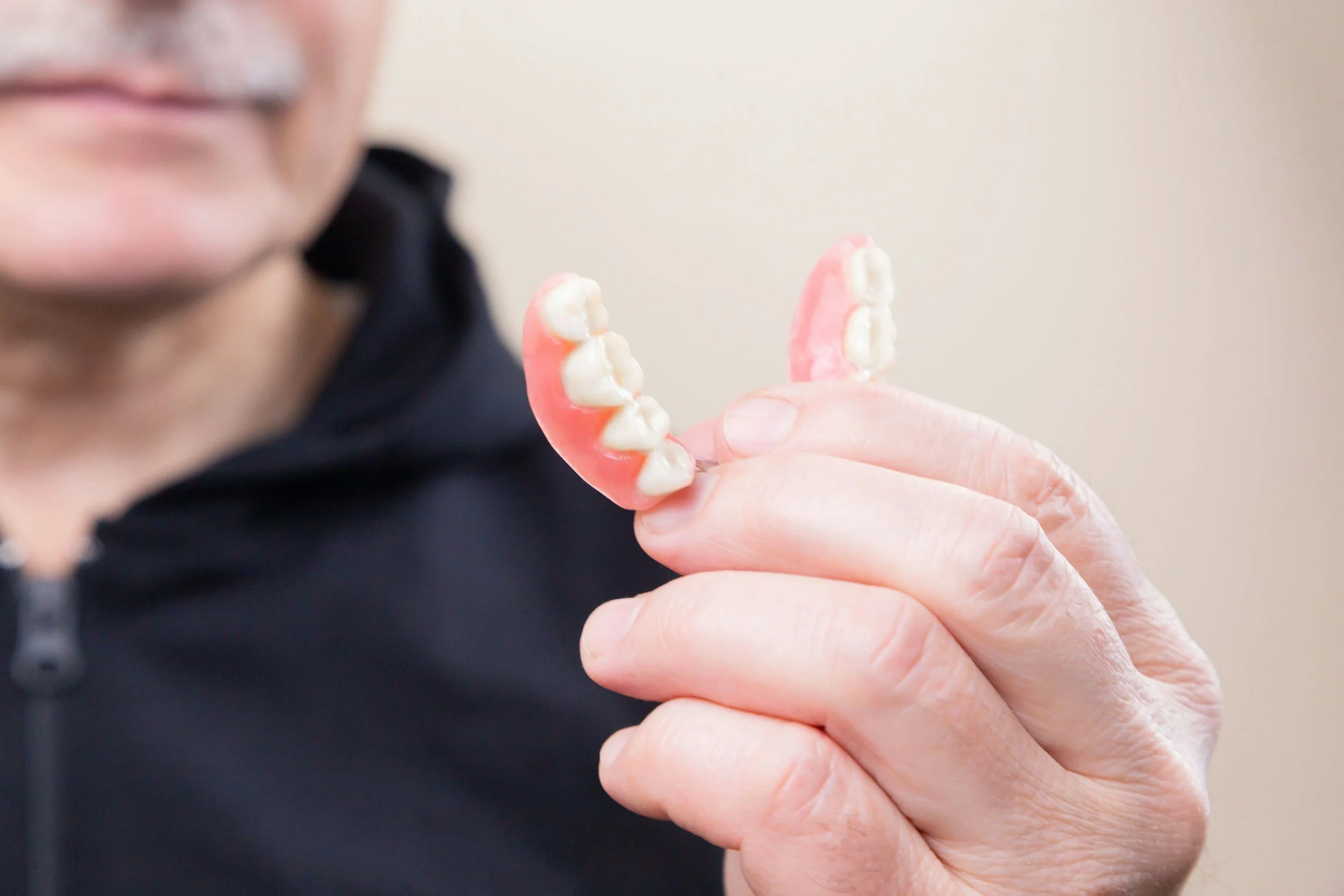 Close-up of an older person's hand holding a pink and white denture with a partial set of teeth.