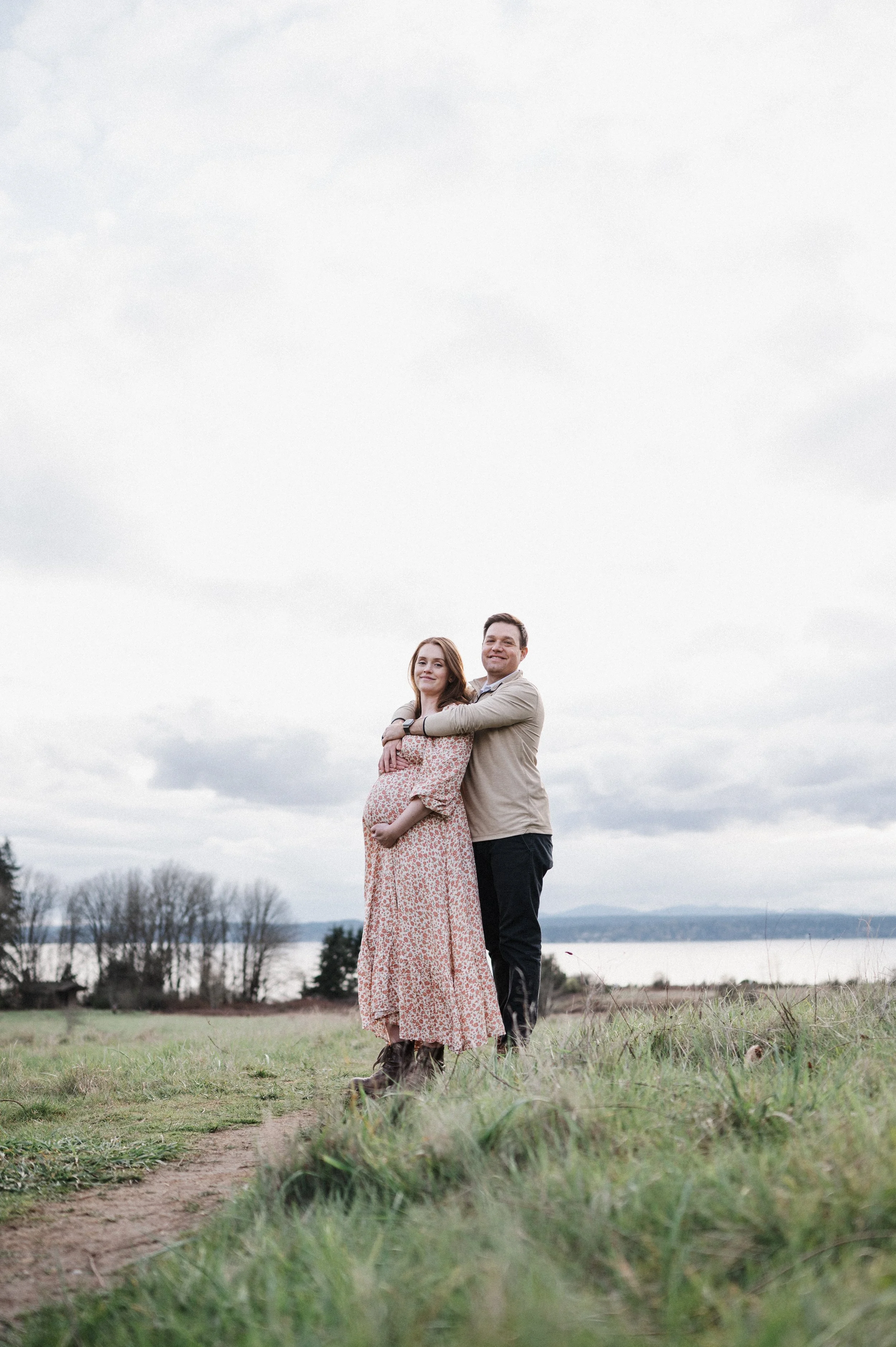 mom to be and dad standing in field at Discovery Park