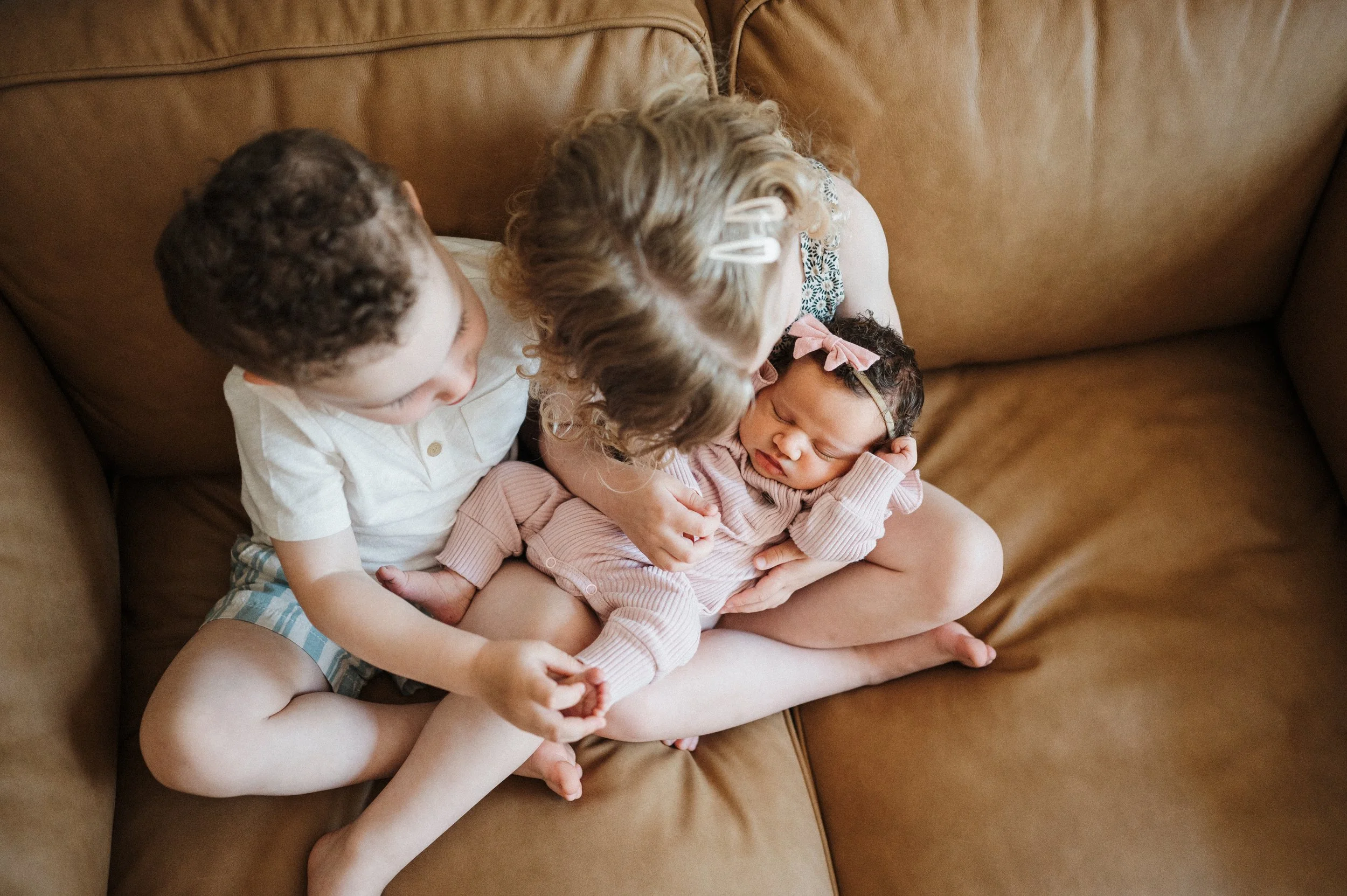 Older siblings holding newborn baby on couch