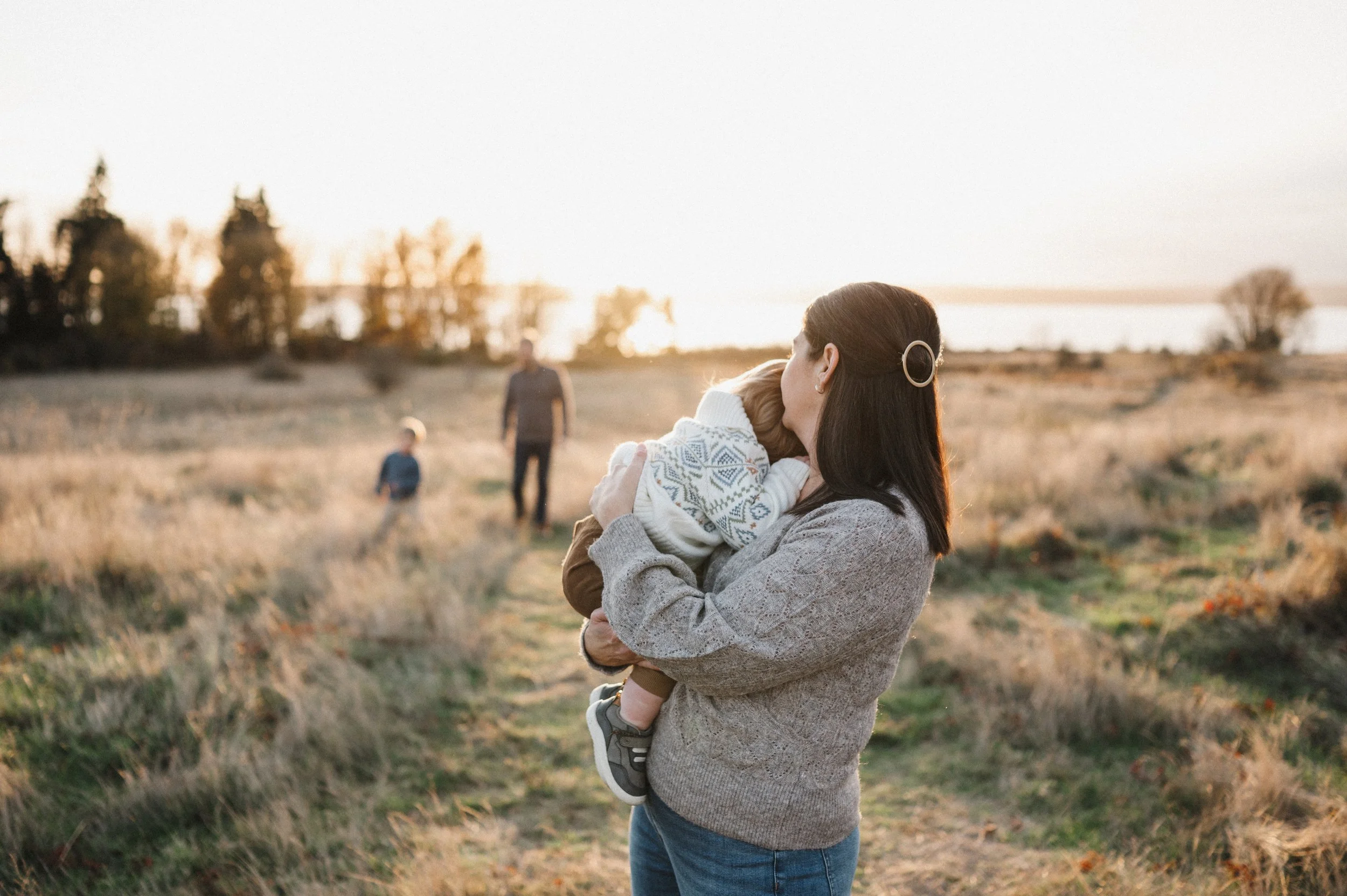 Mom snuggling with baby while dad and toddler play together in the background