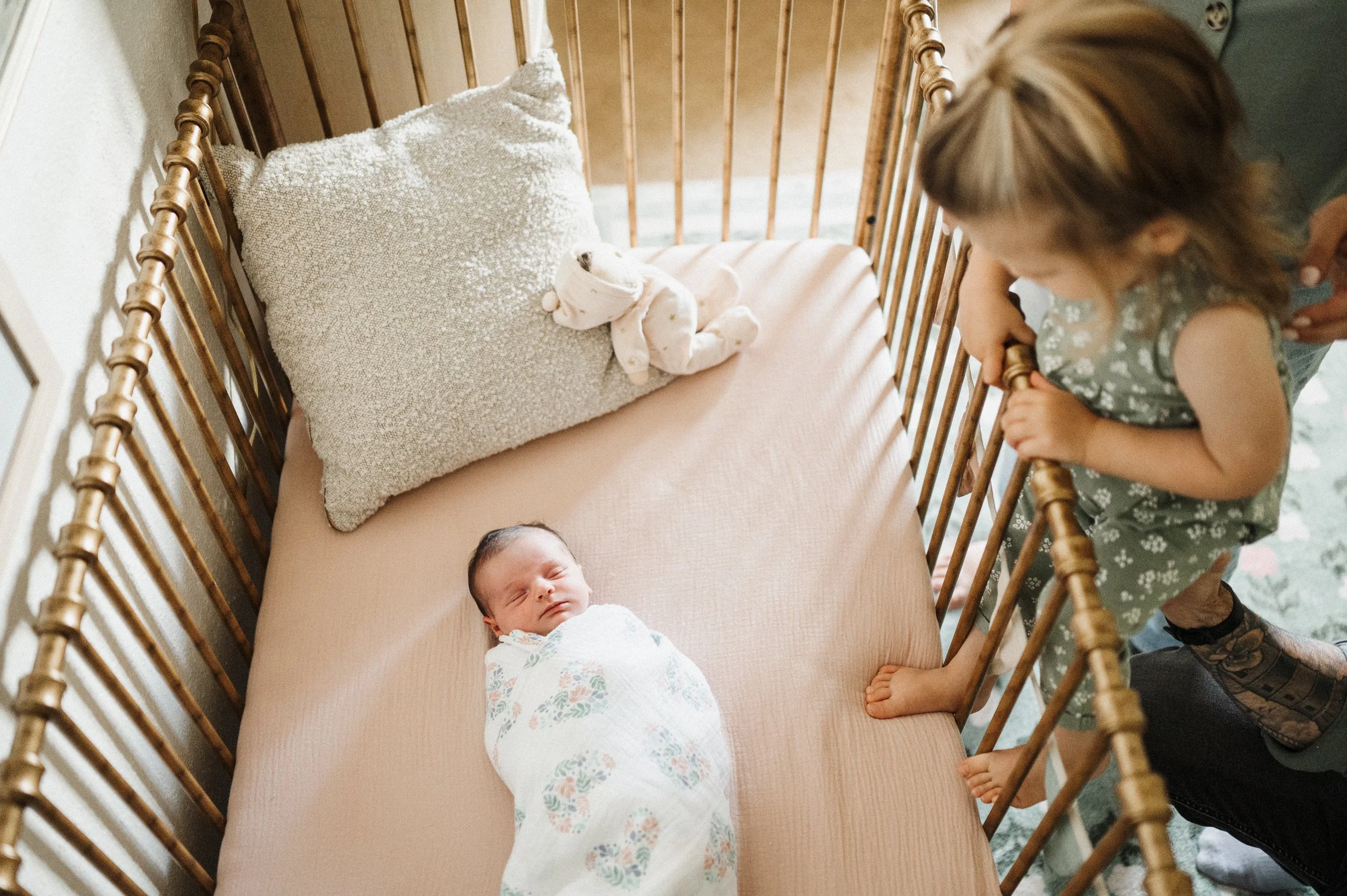 Newborn lying in crib while big sister looks over her