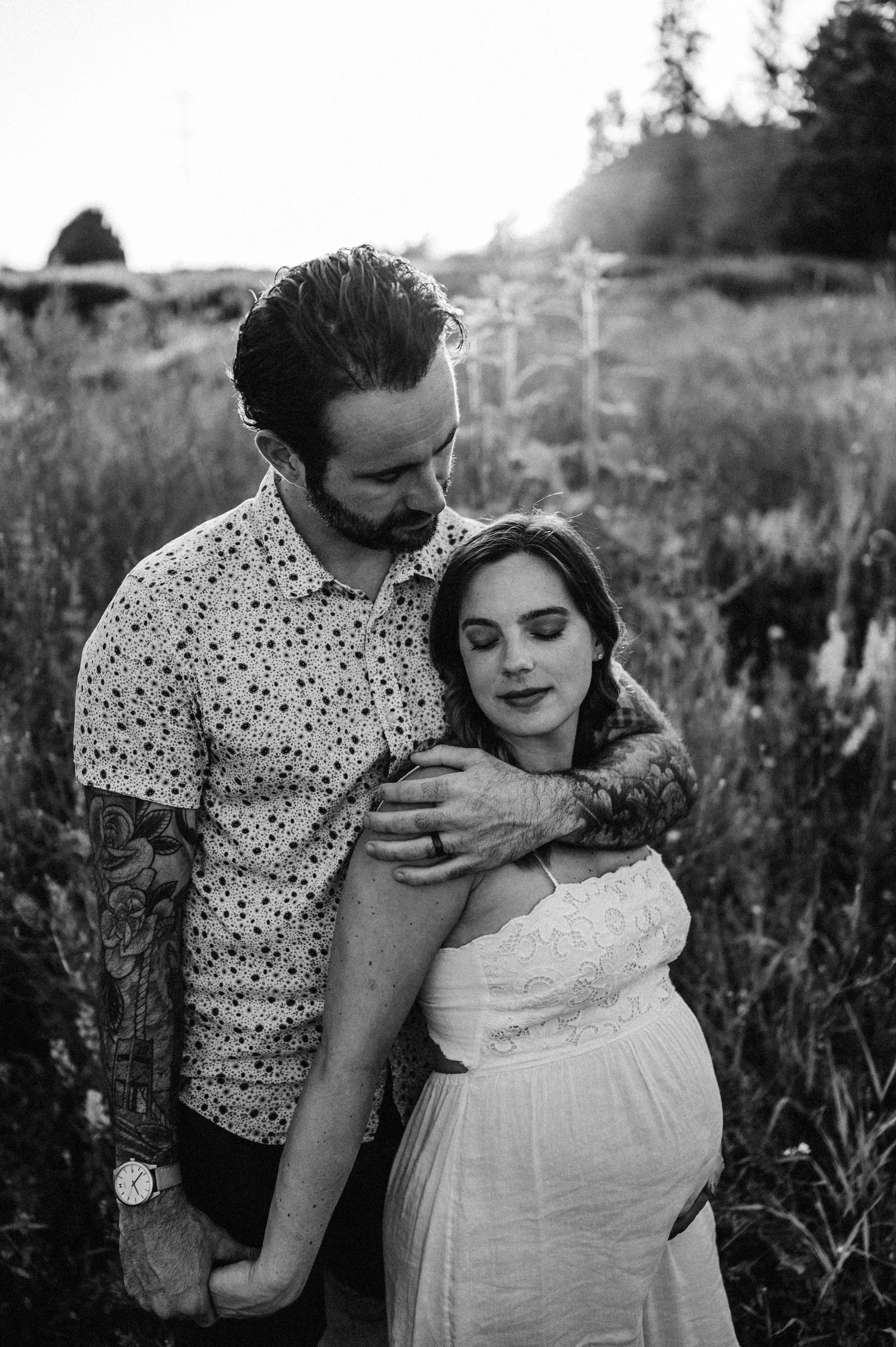 pregnant woman and husband standing in field