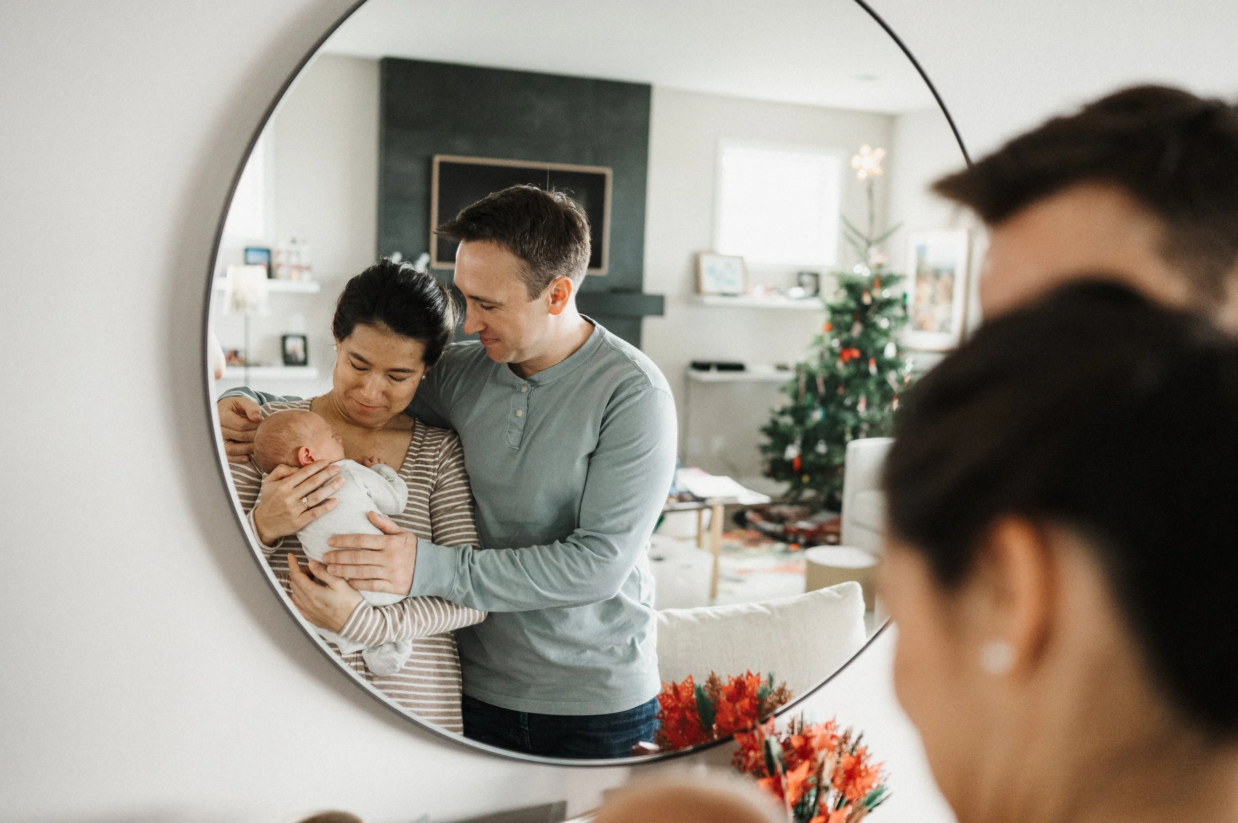 Mom and dad holding newborn in front of mirror