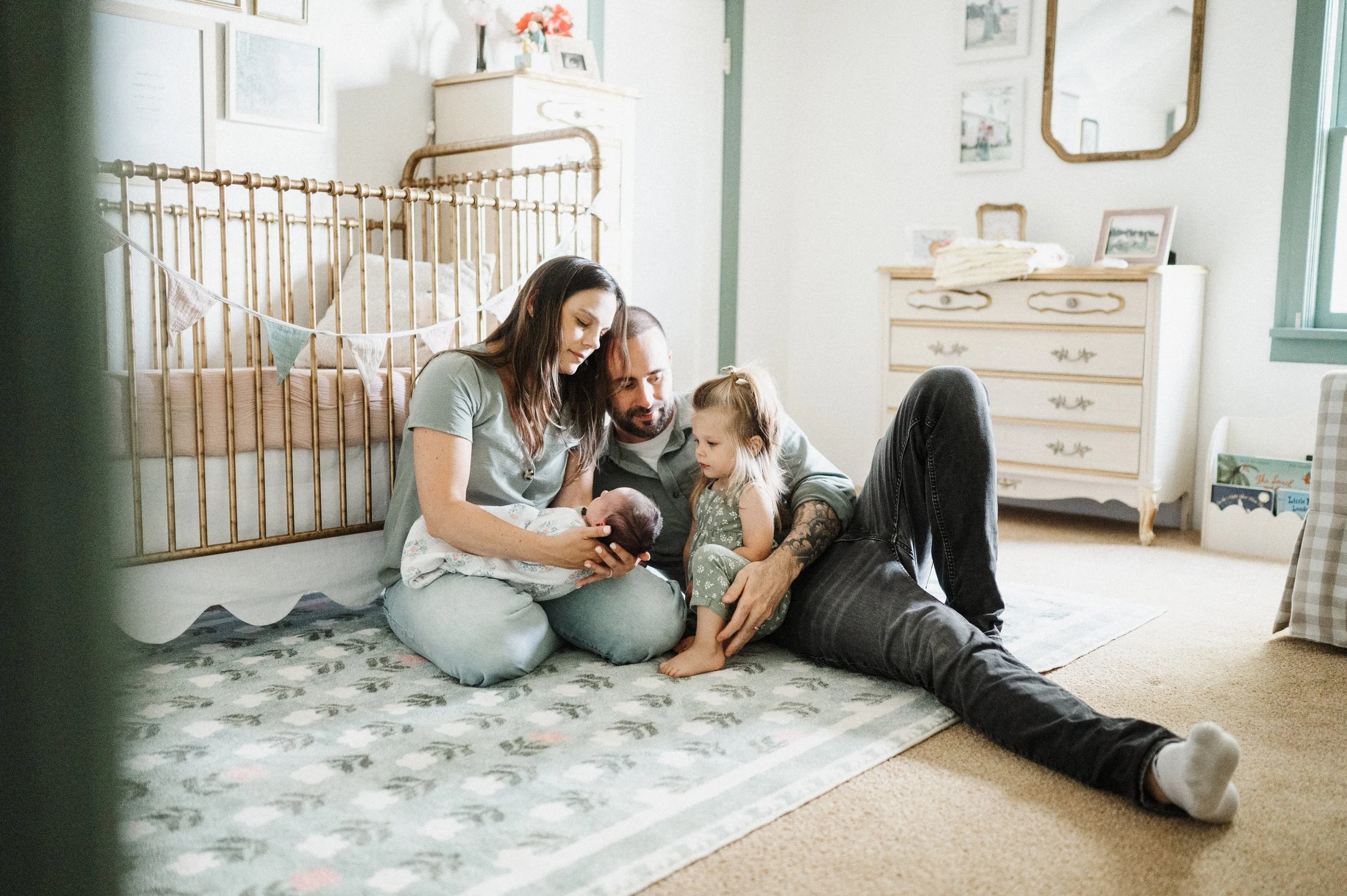Mom, Dad, big sister, and newborn sit by crib during lifestyle photo session