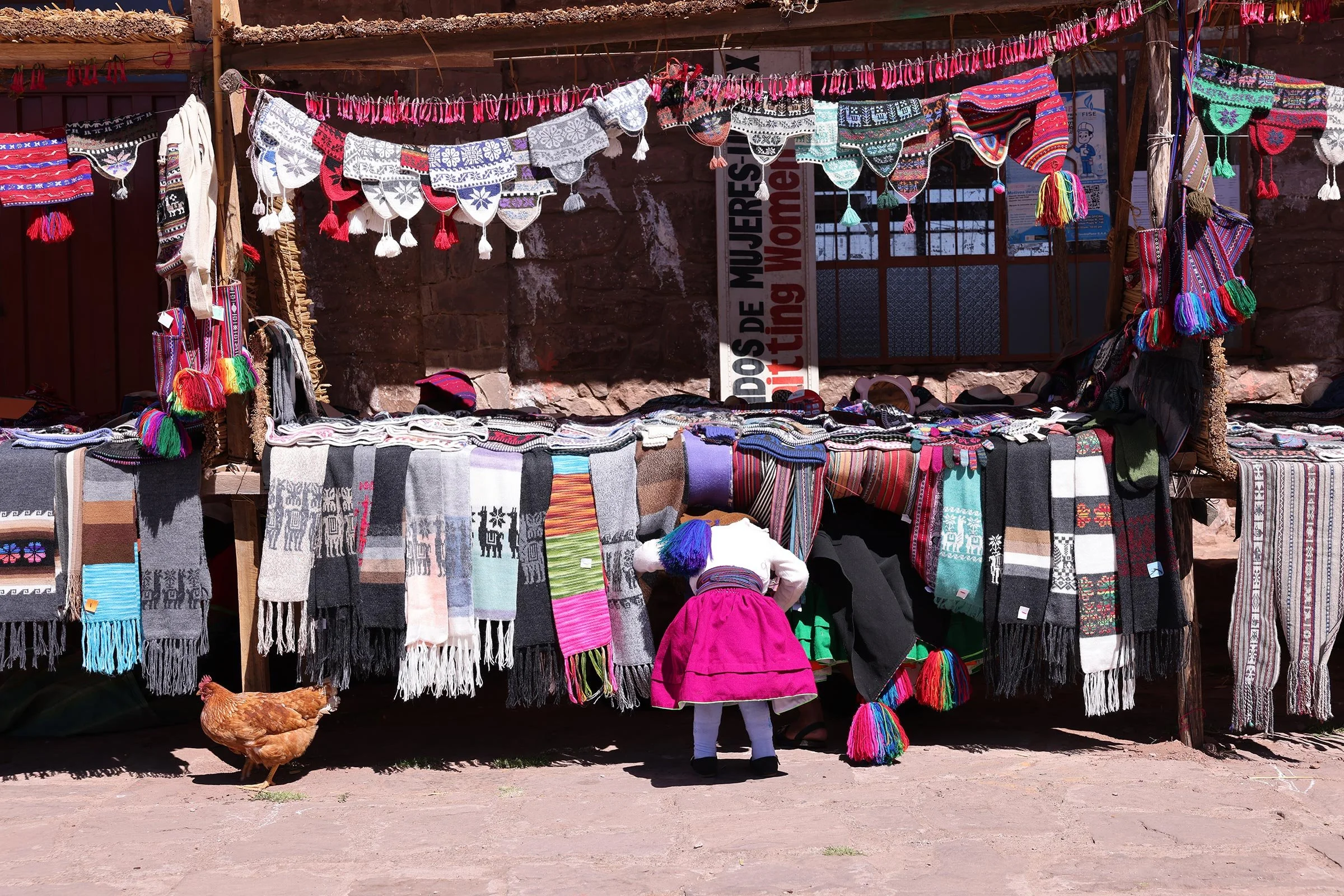 Lokalt andinskt hantverk till försäljning på ön Taquile och en flicka i rosa kjol som tittar efter en höna som passar på att smita därifrån