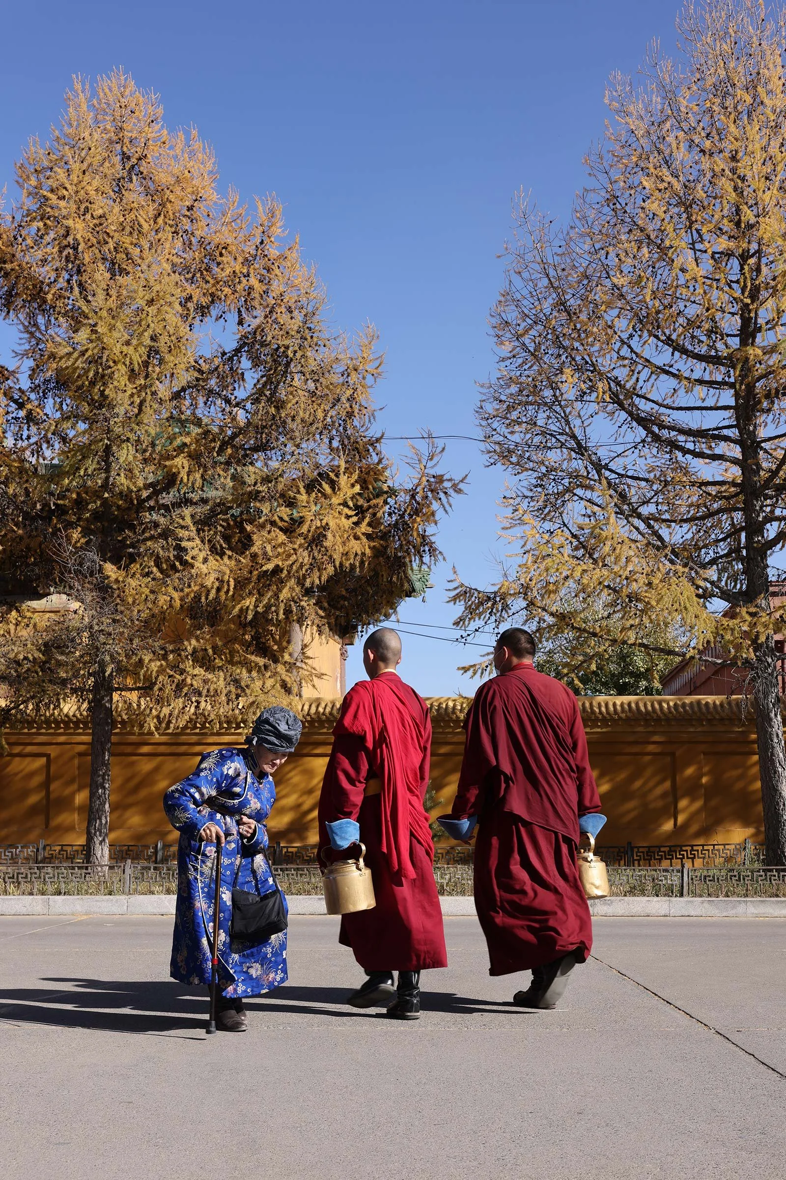  Två munkar i röda dräkter och en äldre dam i blå klänning vid Gandantegchinlen-klostret, ett buddhistiskt kloster i Ulaanbaatar, Mongoliet 