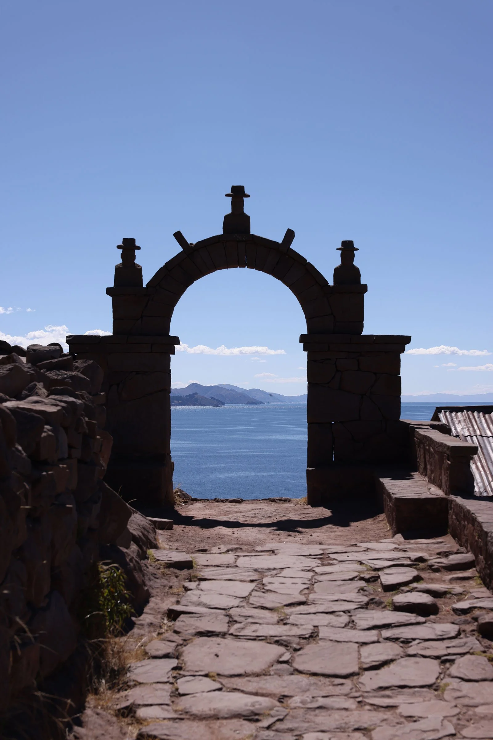 En stenbåge över en gångväg i sten på ön Taquile, med utblick över Titicacasjön, Peru