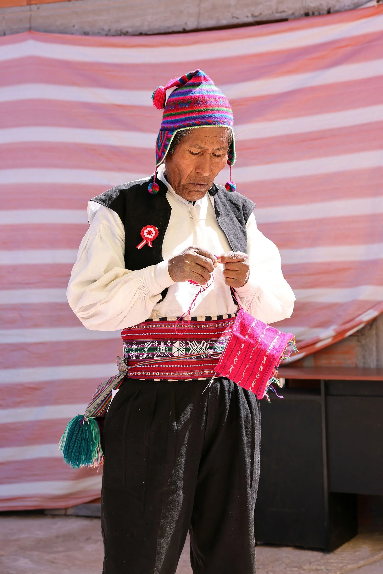 Alejandro, en taquileños, står upp i traditionella kläder och visar hur han arbetar med textilhantverk på ön Taquile i Titicacasjön, Peru