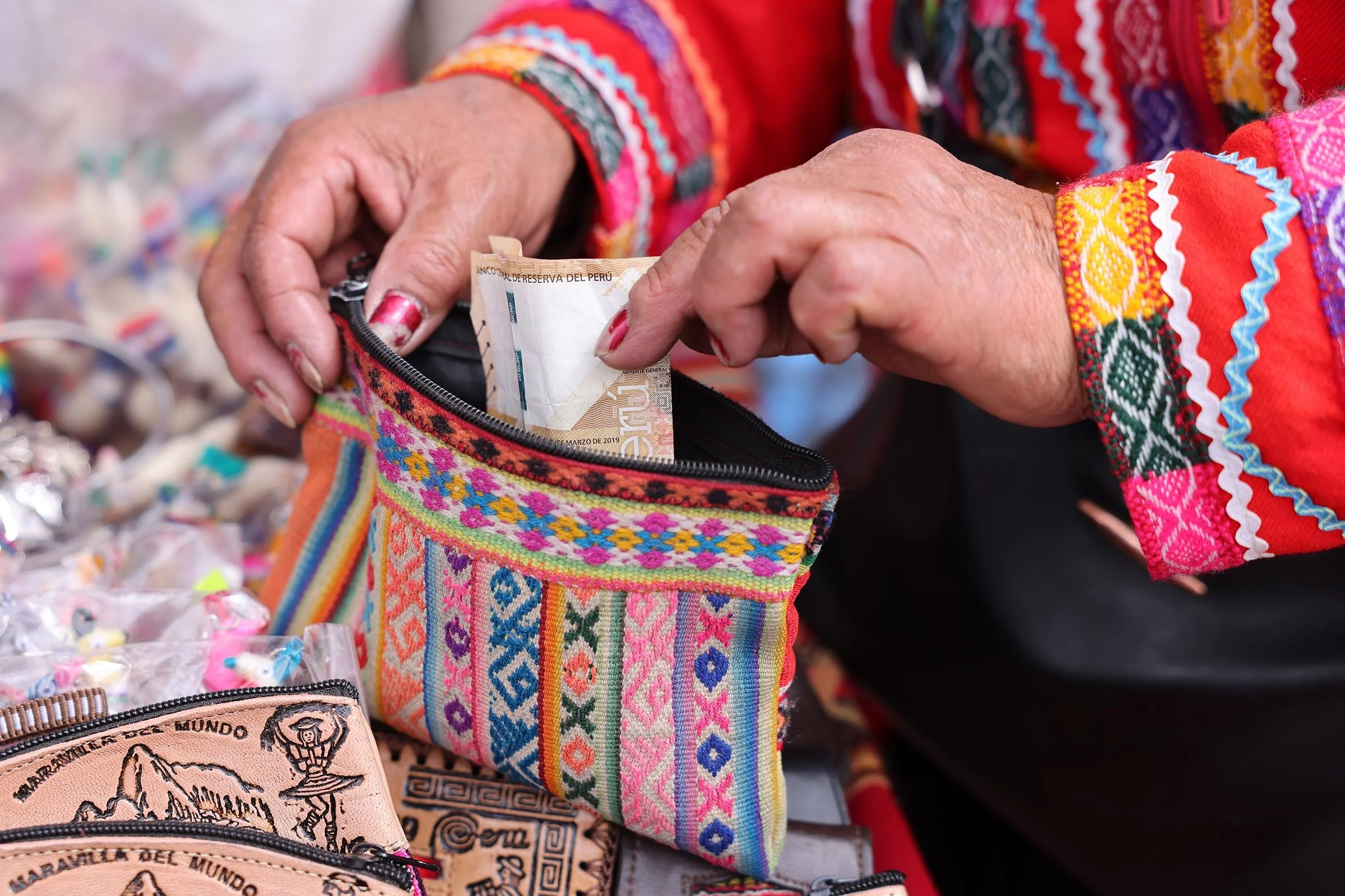 En kvinna lägger ner peruanska sol i en färgglad börs, Cusco, Peru