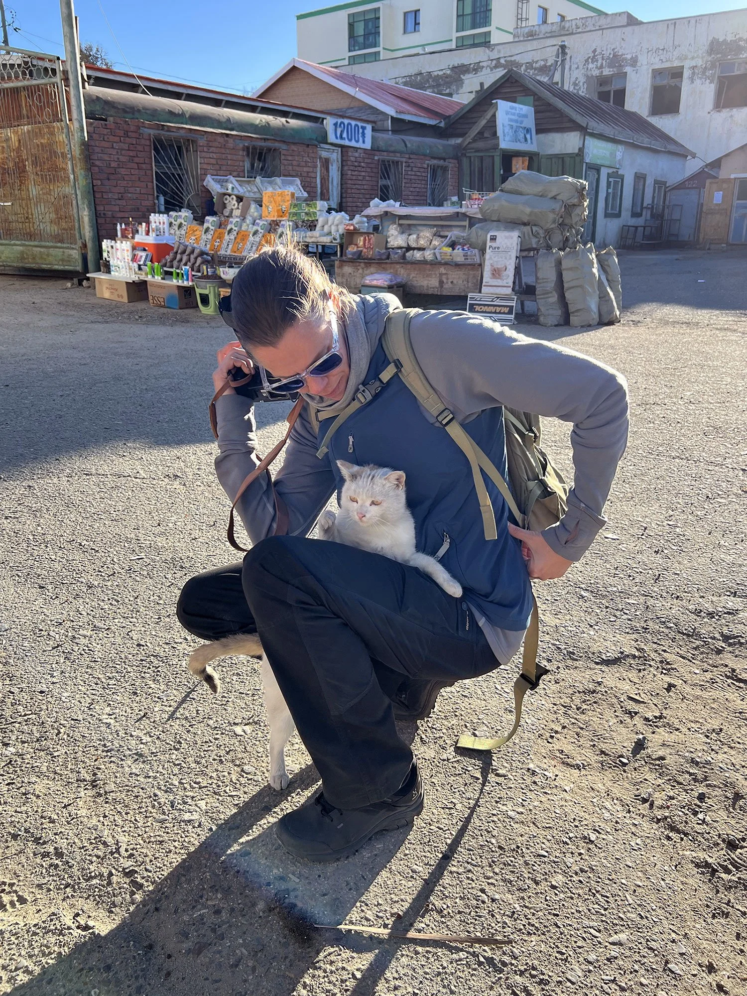 Med en vitspräcklig liten katt i knäet på en dammig asfaltsplan i Kharkhorin, Mongoliet