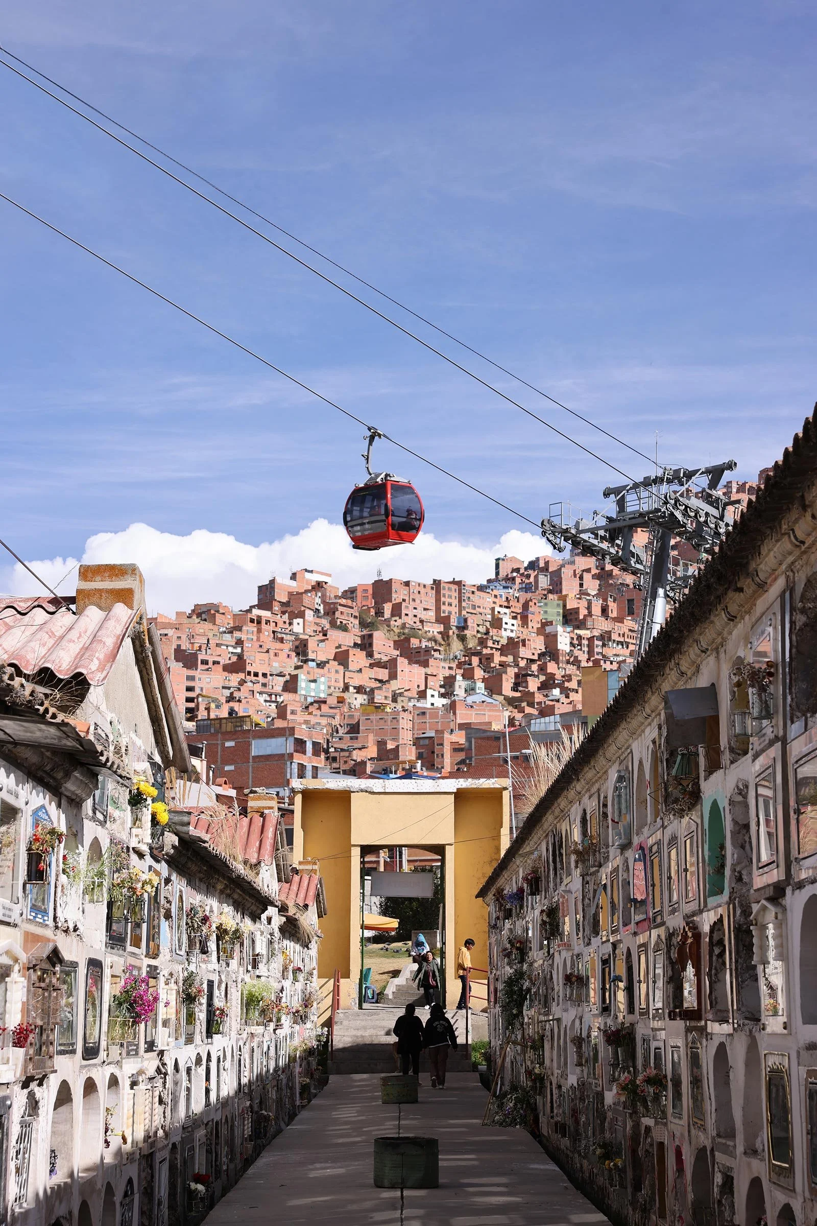 En av gångarna på kyrkogården Cementerio General de La Paz med en röd Mi Teleférico ovanför, La Paz, Bolivia