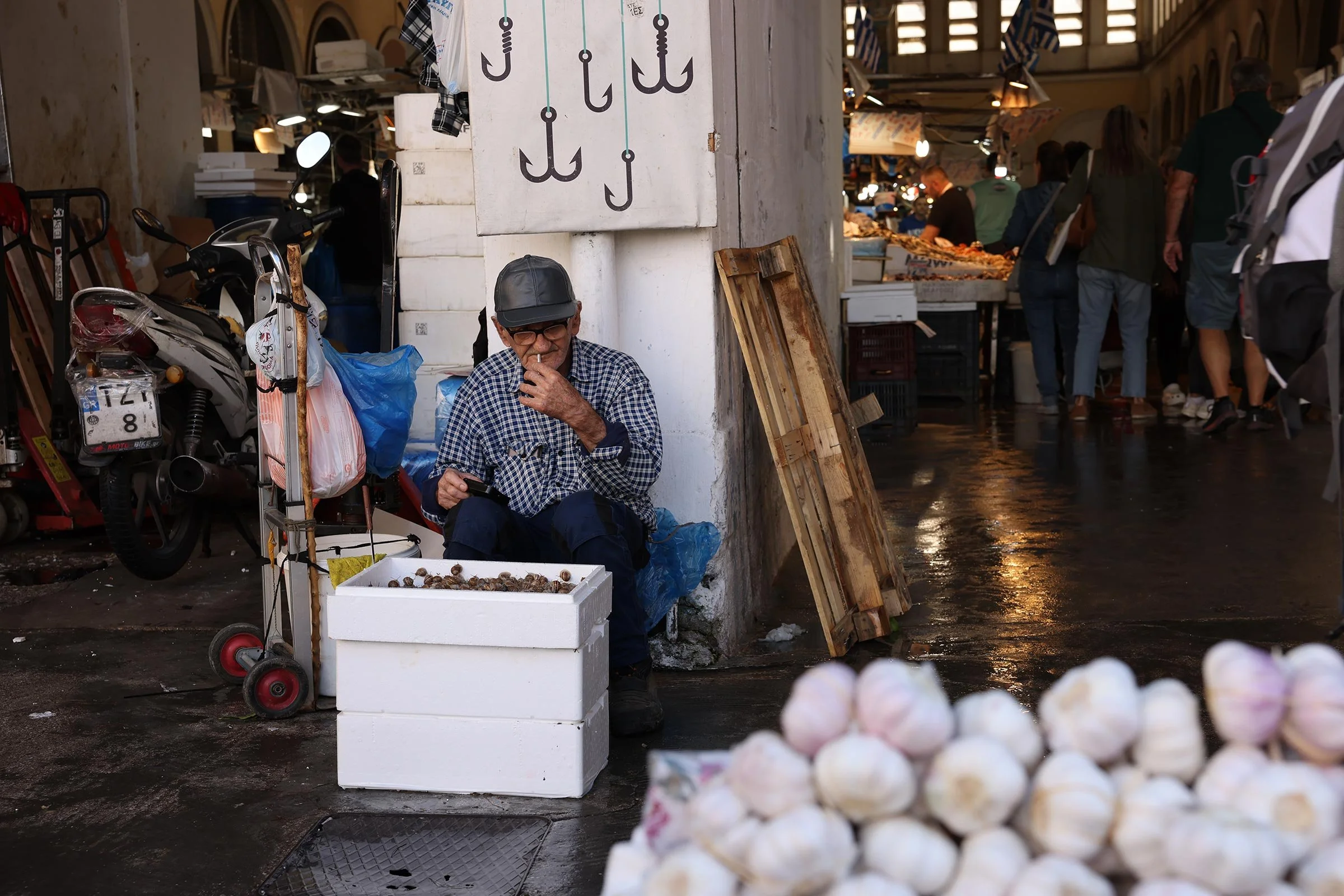 En äldre man i keps sitter utanför Centralmarknaden Varvakios Agora i Aten och säljer sniglar