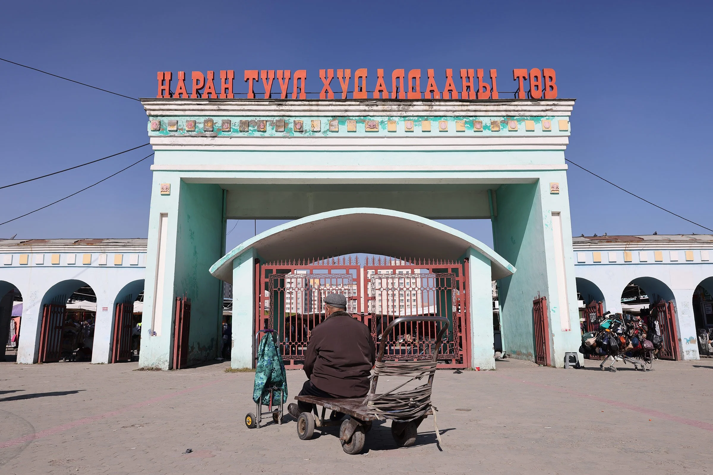 En man som sitter på en kärra utanför entrén till Narantuul Market, Ulaanbaatar, Mongoliet