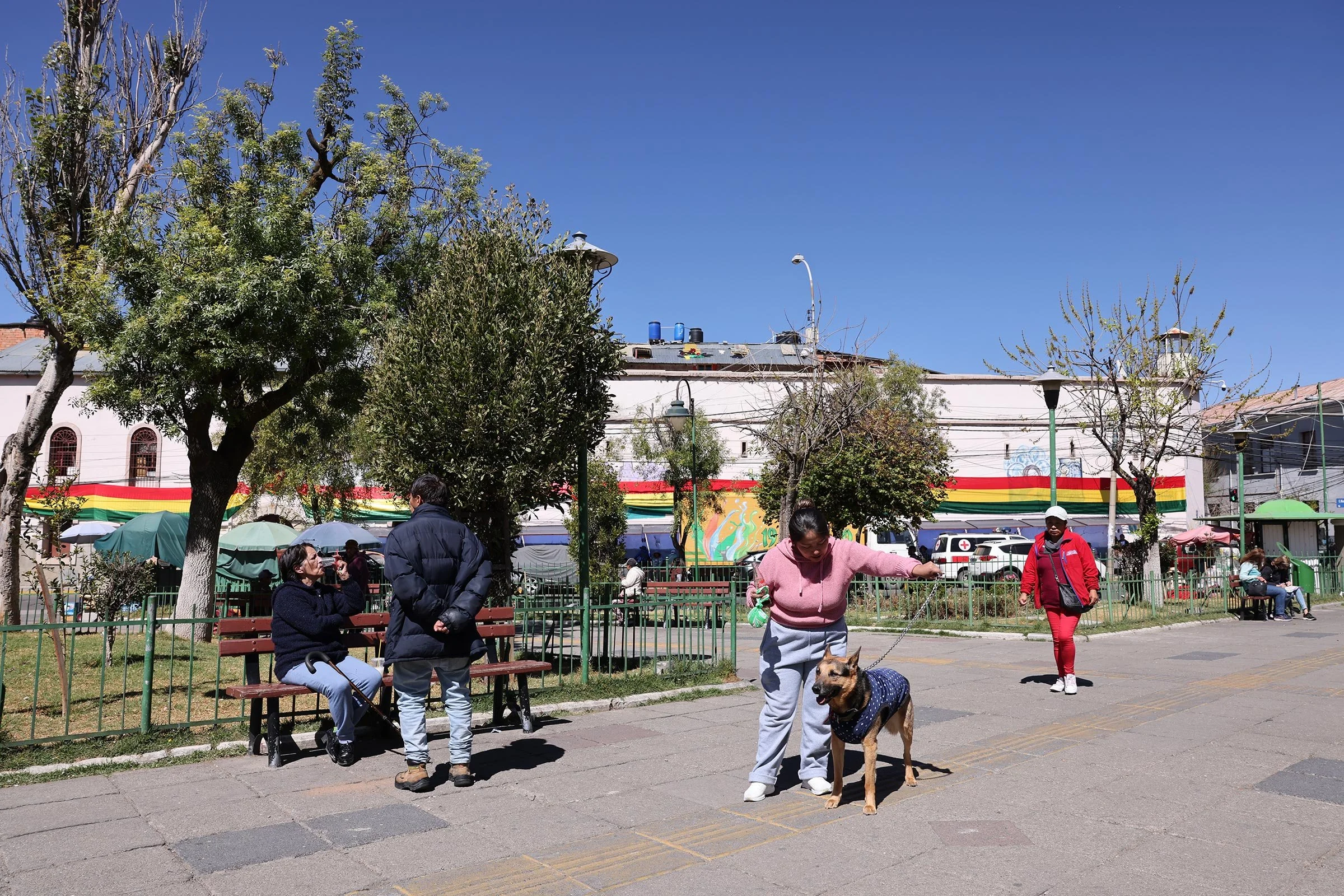 En kvinna med en hund och två personer vid en bänk på Plaza de San Pedro, med fängelset San Pedro i bakgrunden, La Paz, Bolivia