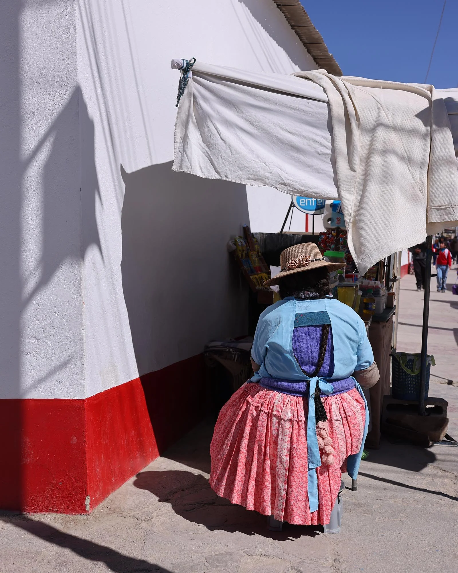 Kvinna i traditionella kläder sitter i ett gatuhörn i Uyuni och säljer dricka och godis, Bolivia