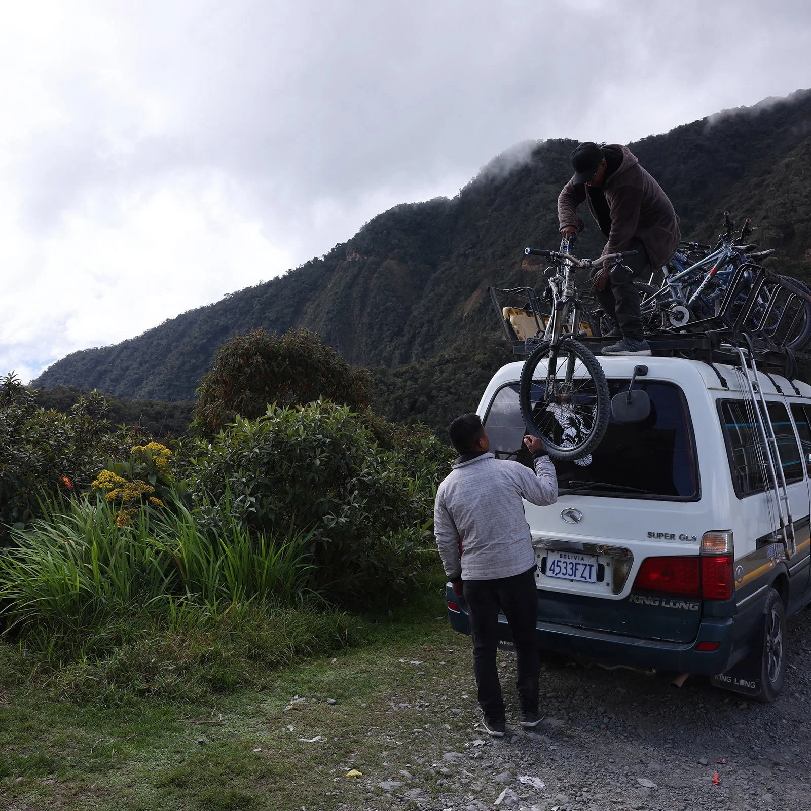 Två män hjälps åt att få upp mountainbikes på ett minibusstak vid Dödens väg i Bolivia