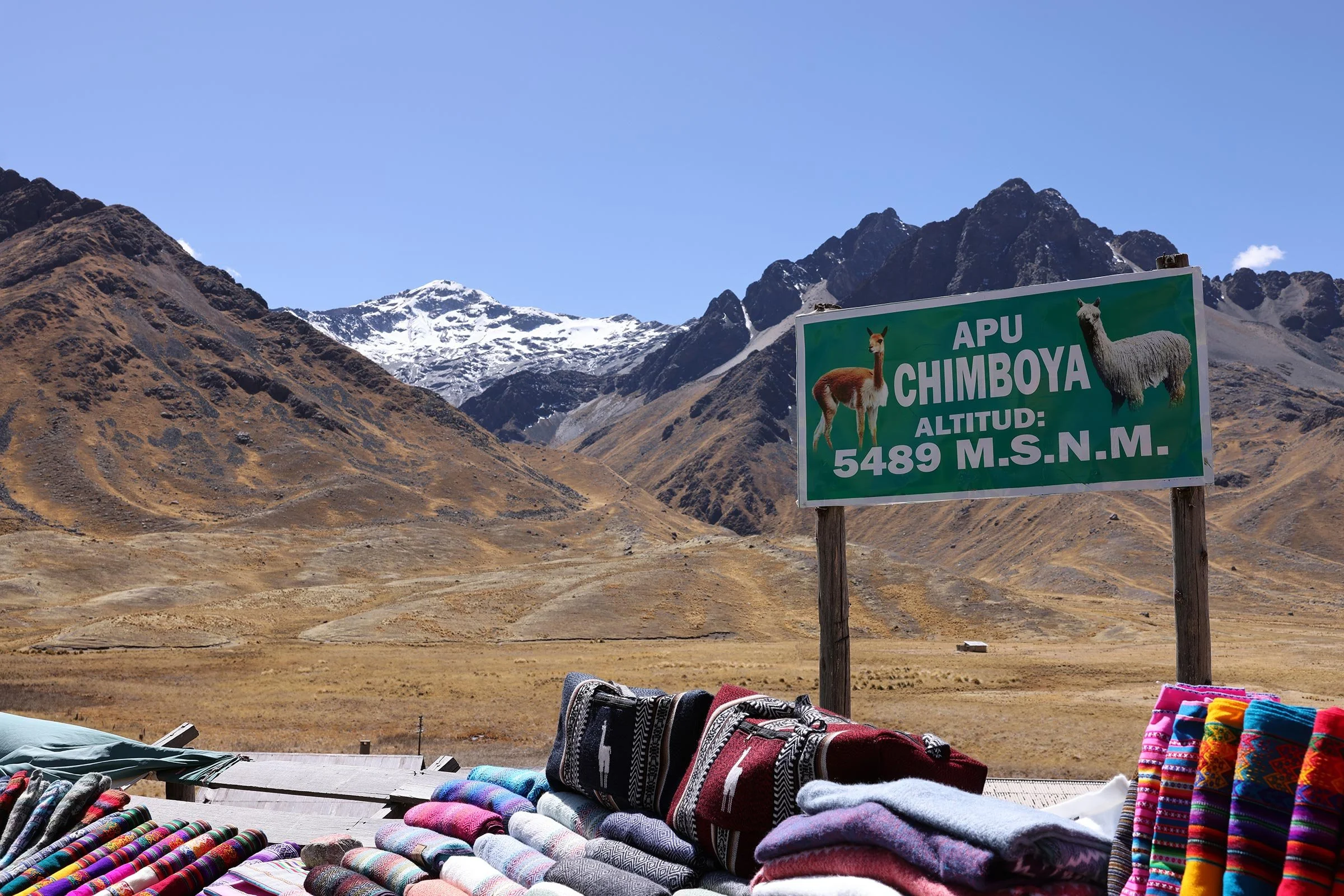Snöklädda bergstoppar och försäljning av textiler vid Abra la Raya-passet, Peru
