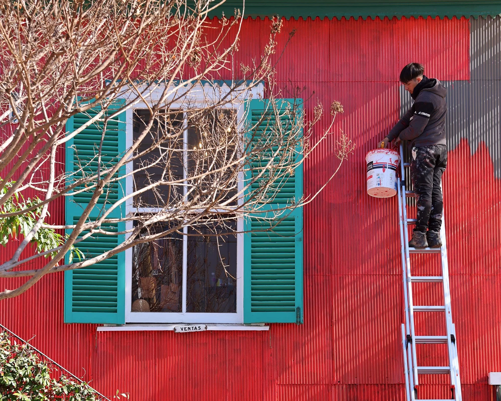 Målare på stege som målar ett hus rött i Valparaiso, Chile