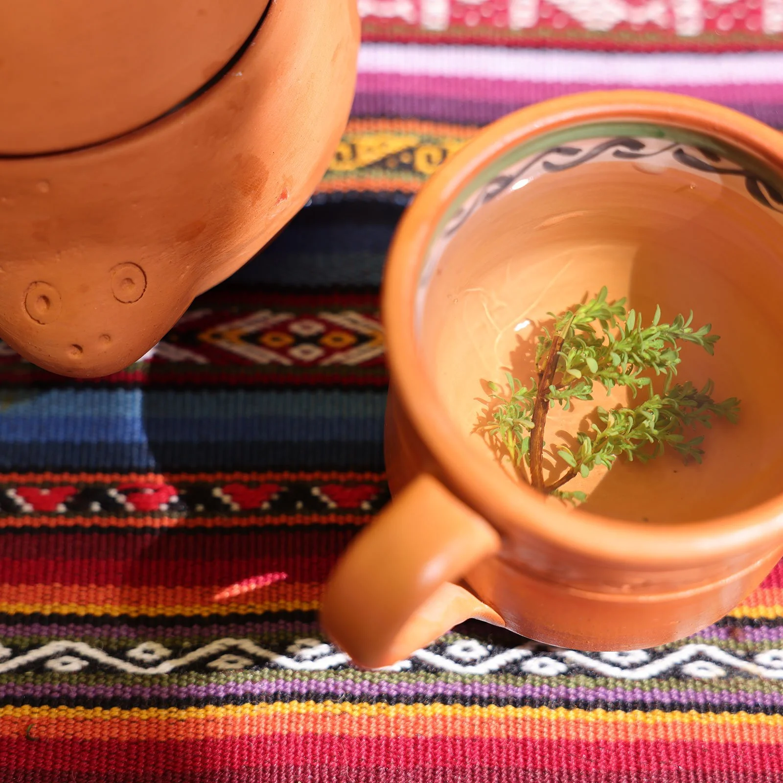 Muña-te, ett traditionellt örtte från Anderna, i en mugg av lera på en vävd, färgglad duk