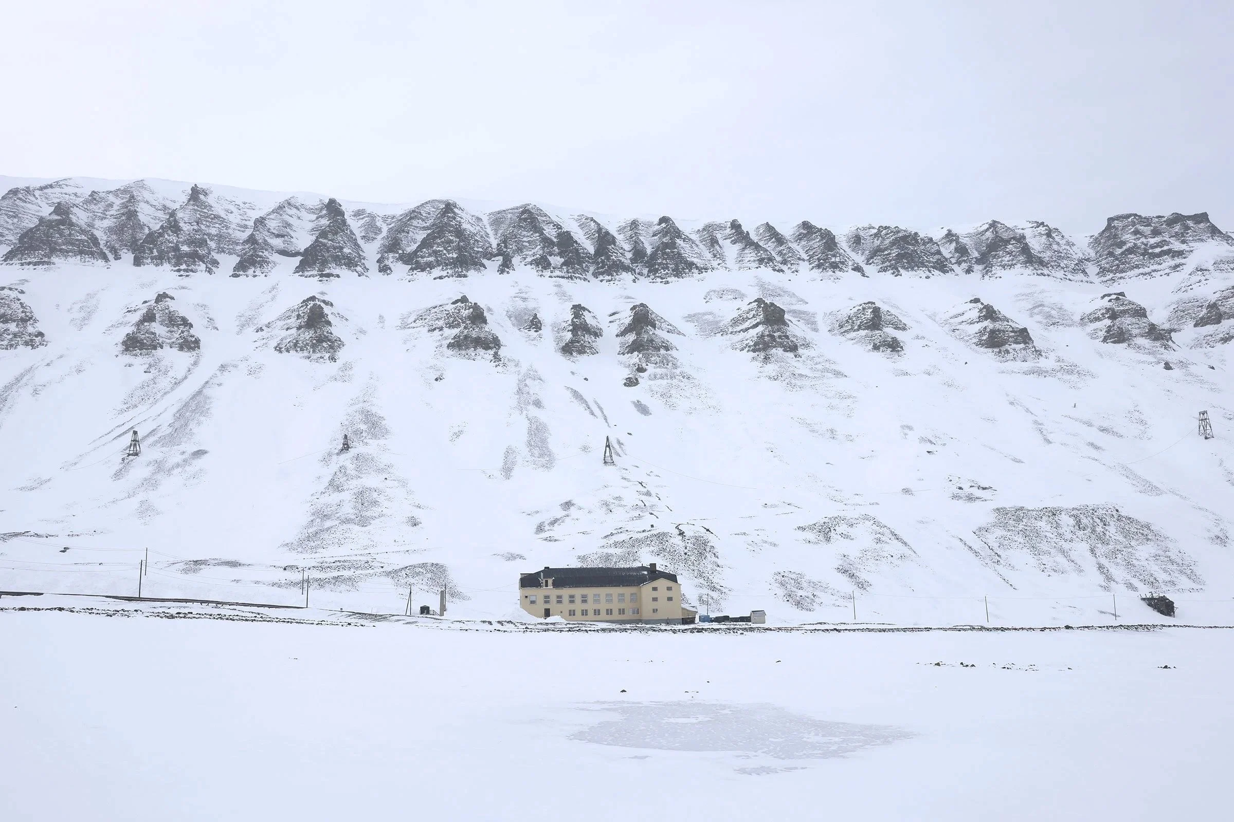 Snöklädda berg, bergstoppar och ett gult hus utanför Longyearbyen, Svalbard