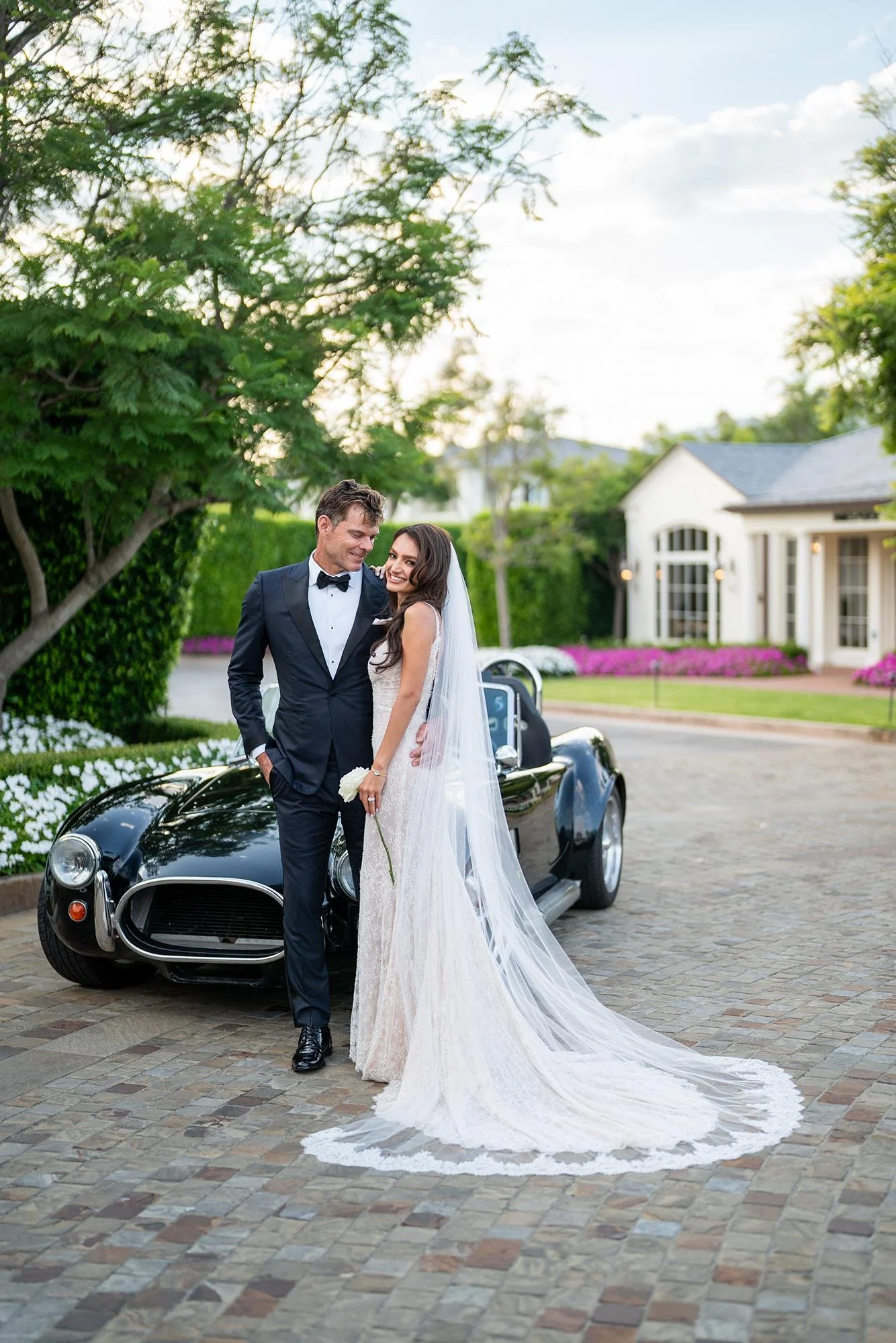 Wedding portraits of the bride and groom posing in the driveway beside a classic car at Rosewood Miramar Beach