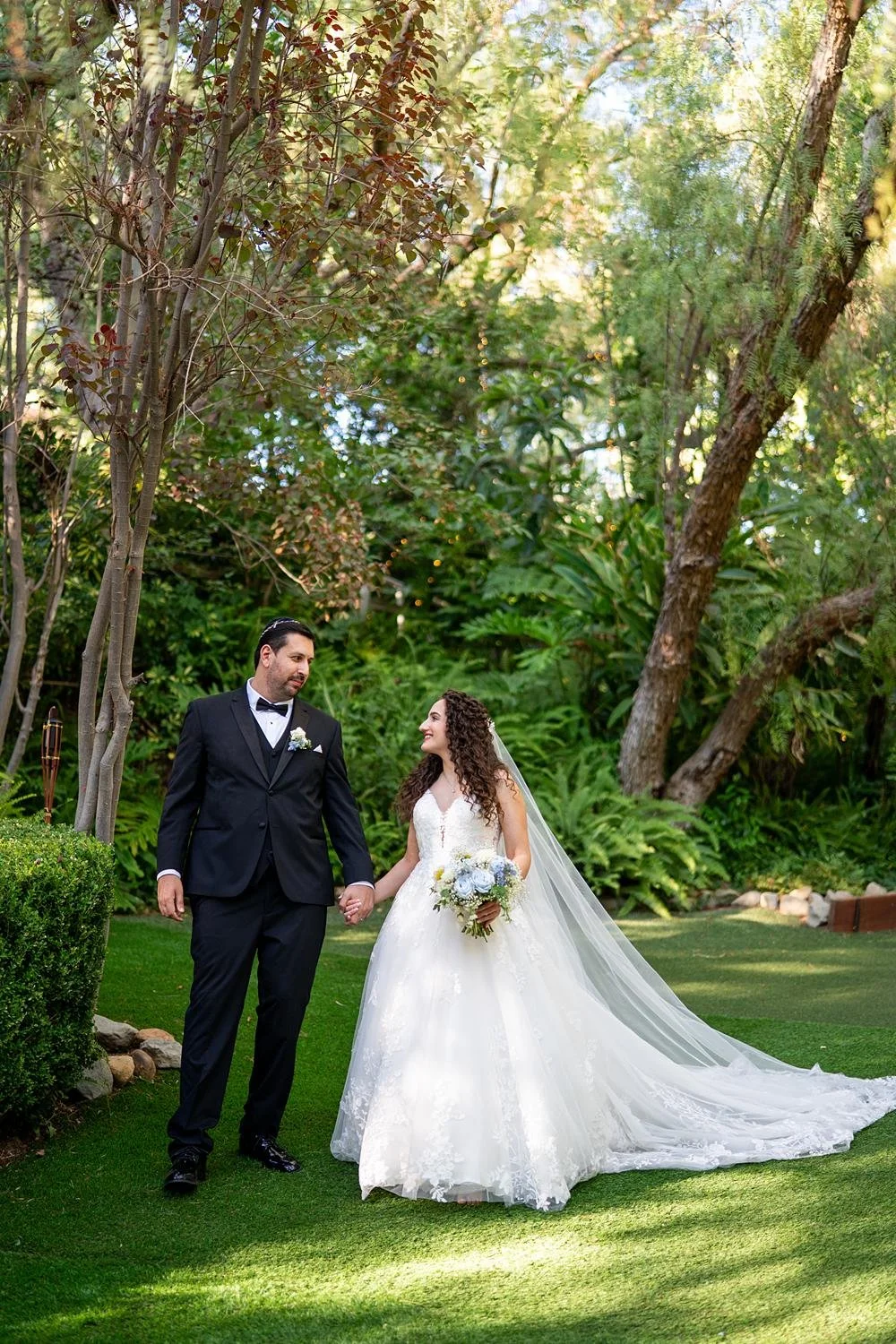 Wedding portraits of bride and groom walking hand-in-hand under trees at The Vineyards Simi Valley