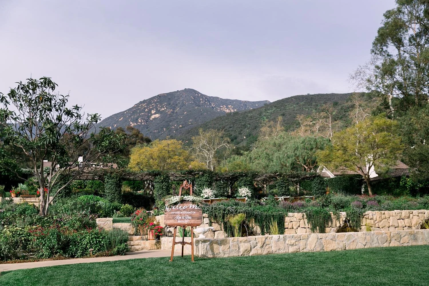Wedding ceremony in Lower Garden with welcome sign and mountain backdrop at San Ysidro Ranch