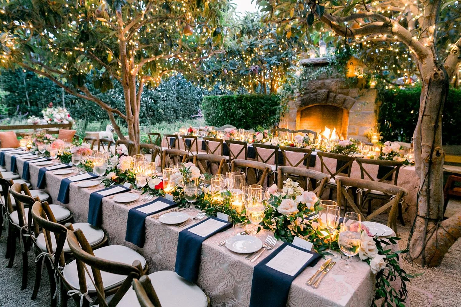 Wedding dinner at Wine Cellar Patio with floral centerpieces, fireplace, and twinkle lights at San Ysidro Ranch