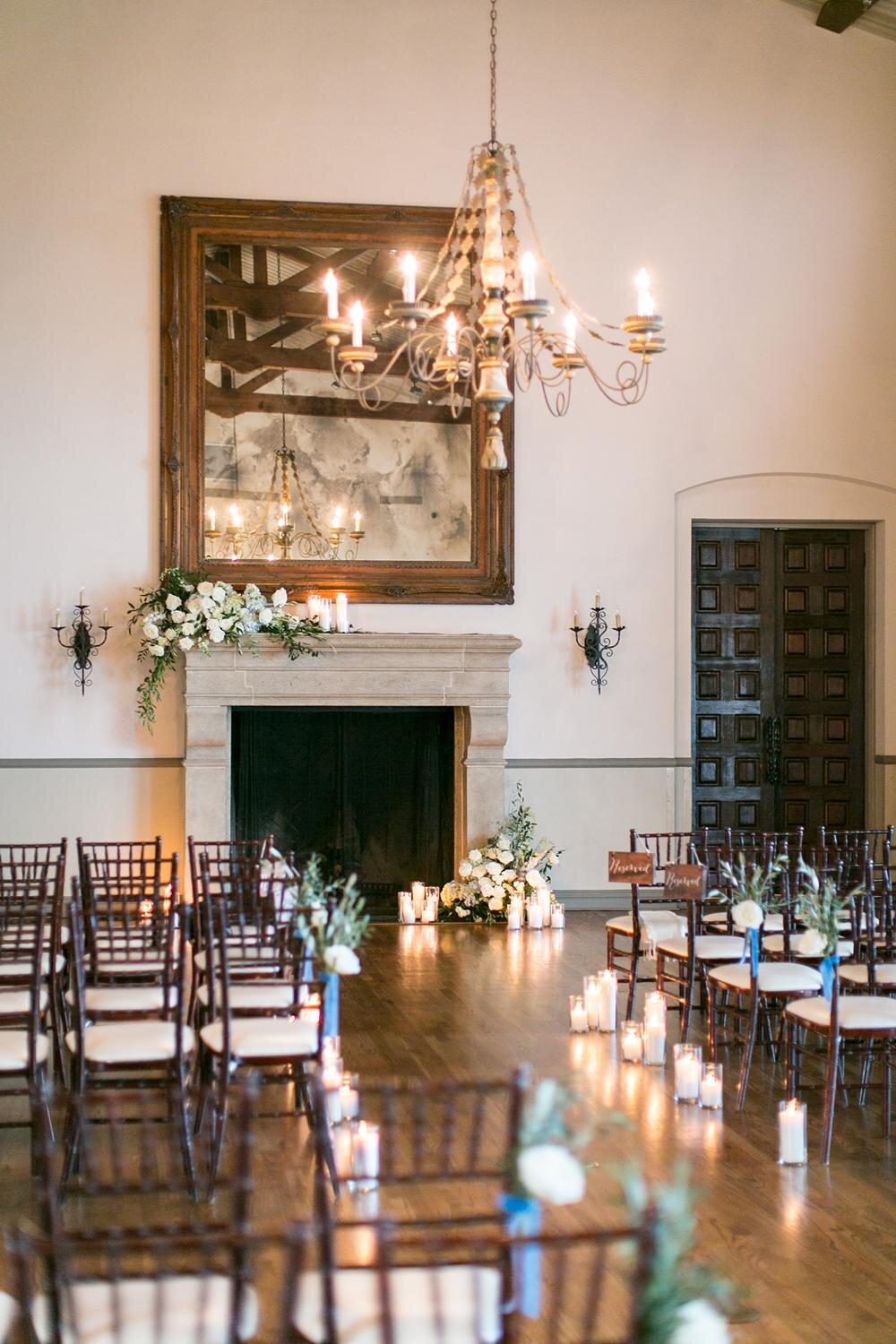 Candlelit aisle and fireplace decorated with florals for a Living Room wedding ceremony at Bel Air Bay Club