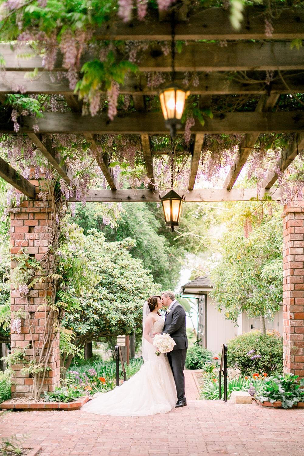 Bride and groom kissing under lilac-lined arbor at Lilly Pond for wedding portraits at Belmond El Encanto