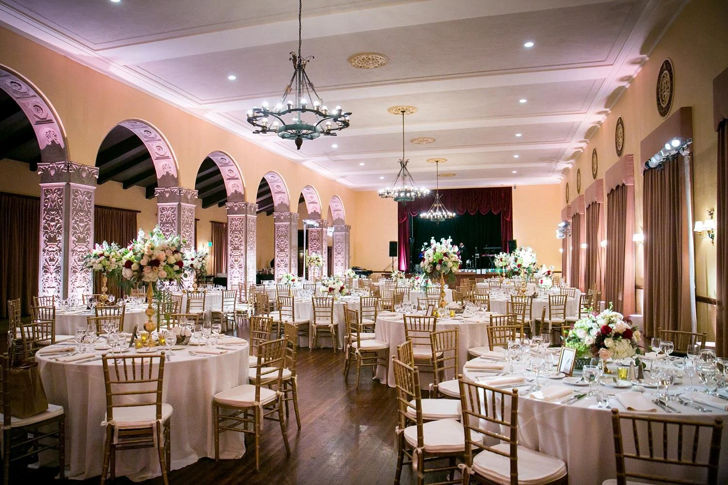 Dining Room wedding reception with low and tall floral centerpieces and lit arches at Ebell of Los Angeles