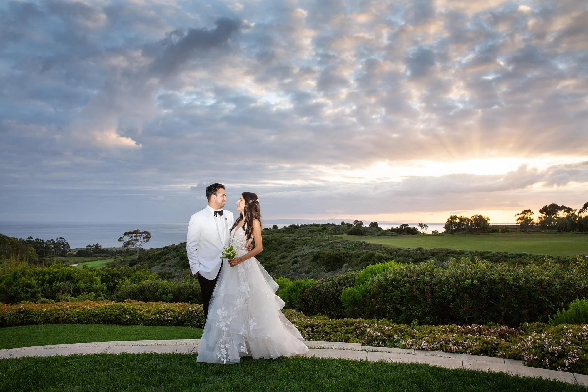 Wedding portraits of bride and groom at sunset with golden rays and dramatic clouds at Pelican Hill