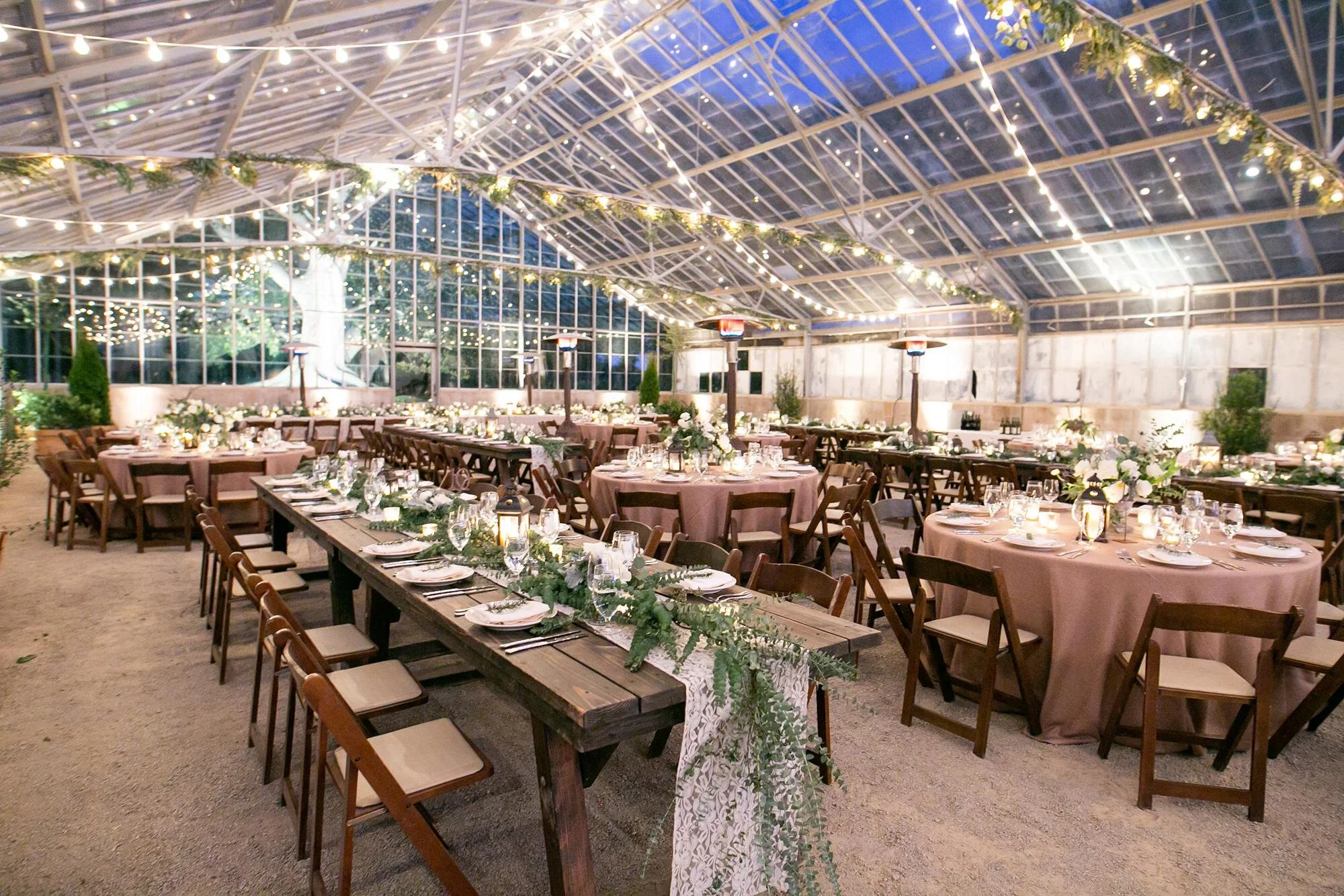 Wedding reception with wooden tables and string lights beneath greenhouse ceiling at Dos Pueblos Orchid Farm