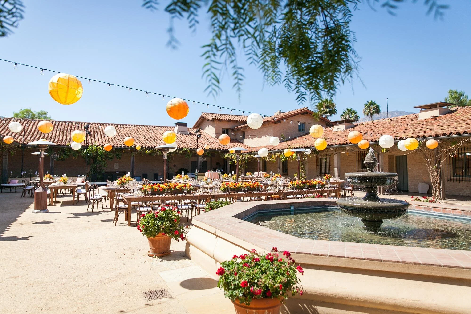 Wedding reception with wooden tables and hanging lanterns in the Santa Barbara Historical Museum Courtyard