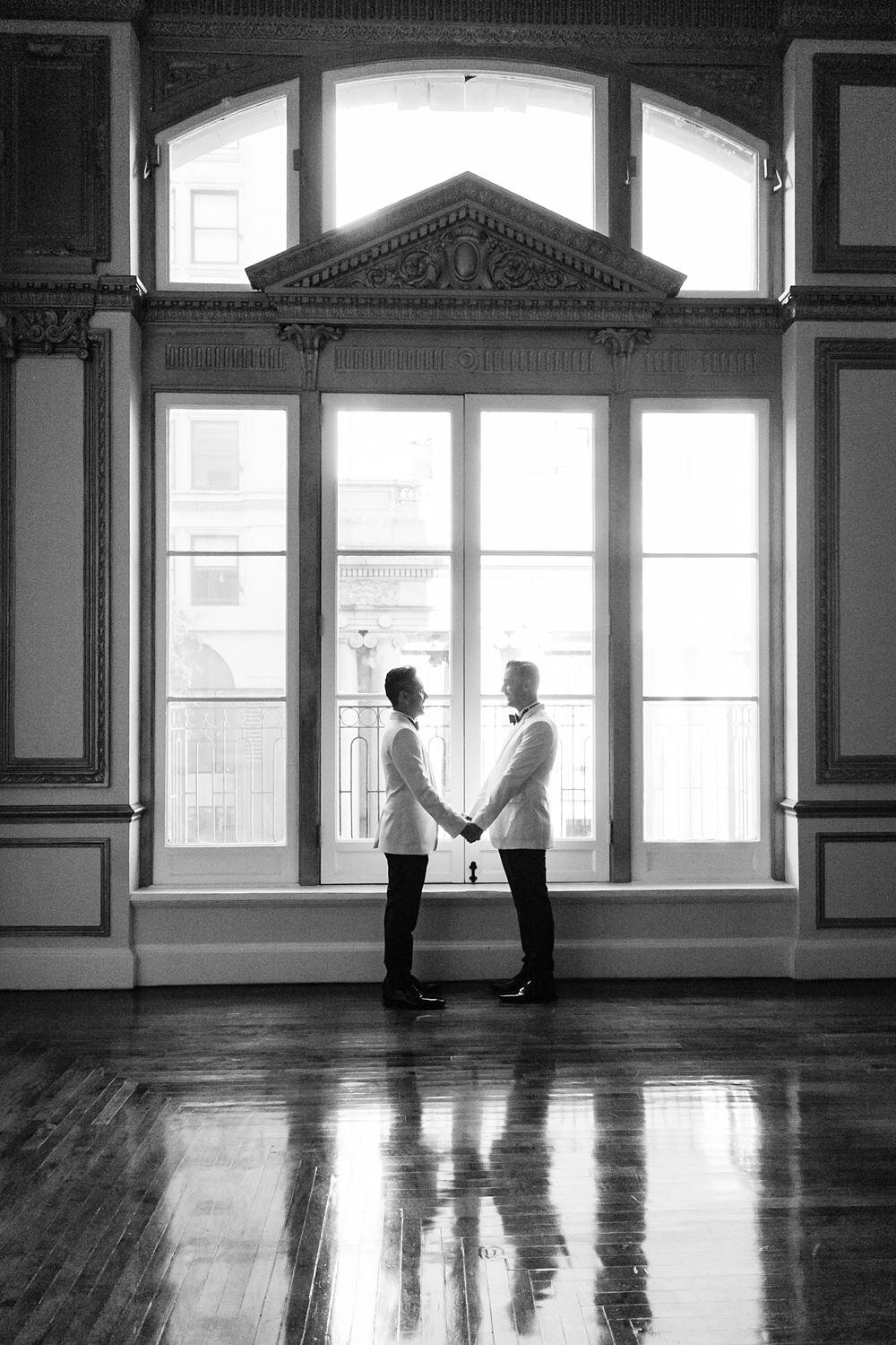 Wedding portrait of grooms silhouetted in a large window at the Alexandria Ballrooms