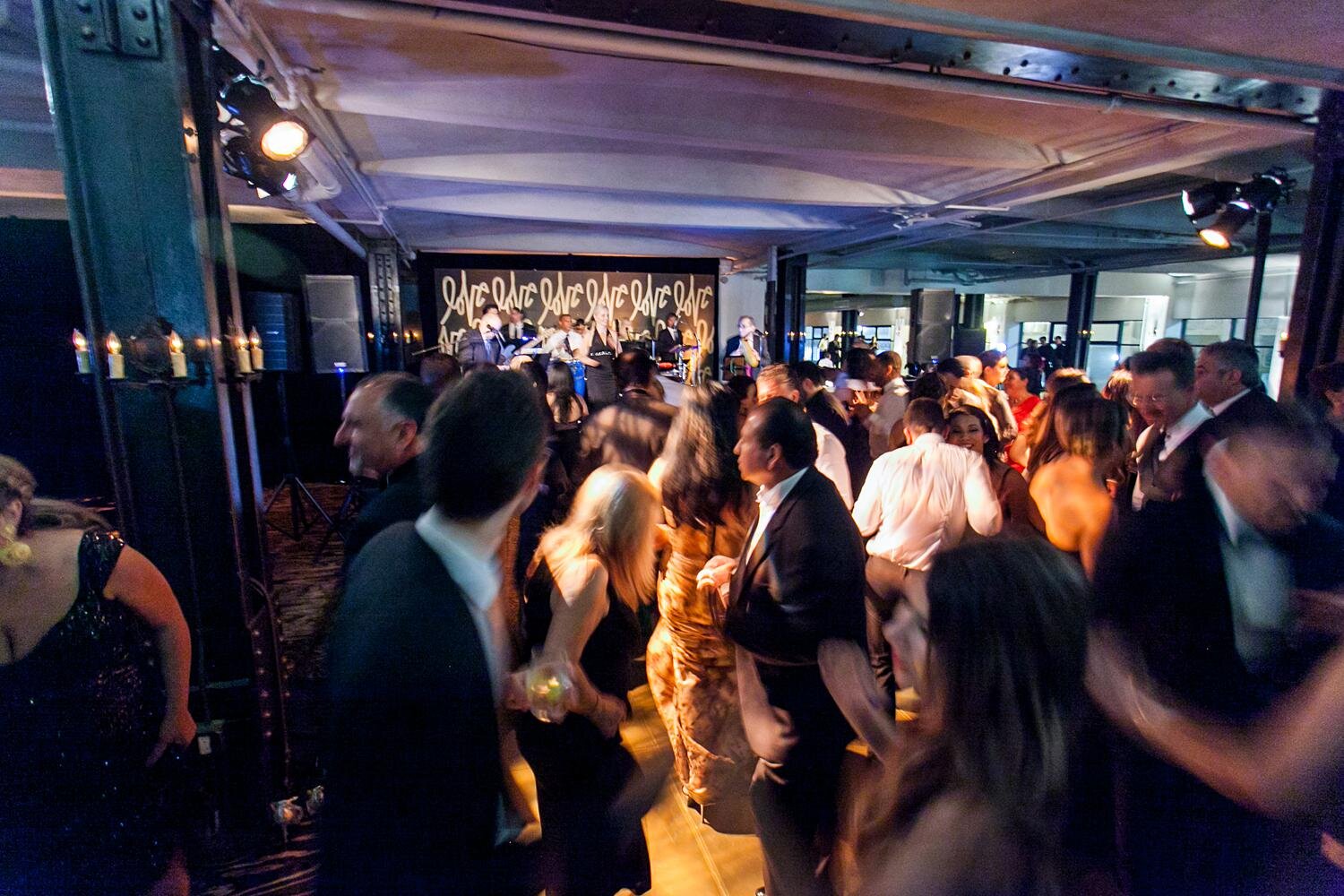 Wedding reception guests dancing in front of a custom band backdrop at the Alexandria Ballrooms