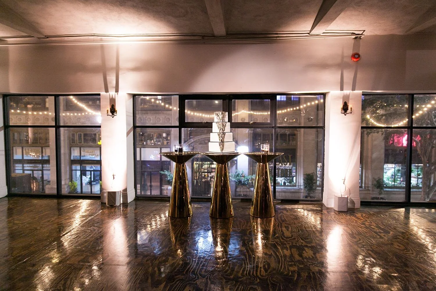 Wedding reception cake displayed on gold tables in front of windows at the Alexandria Ballrooms