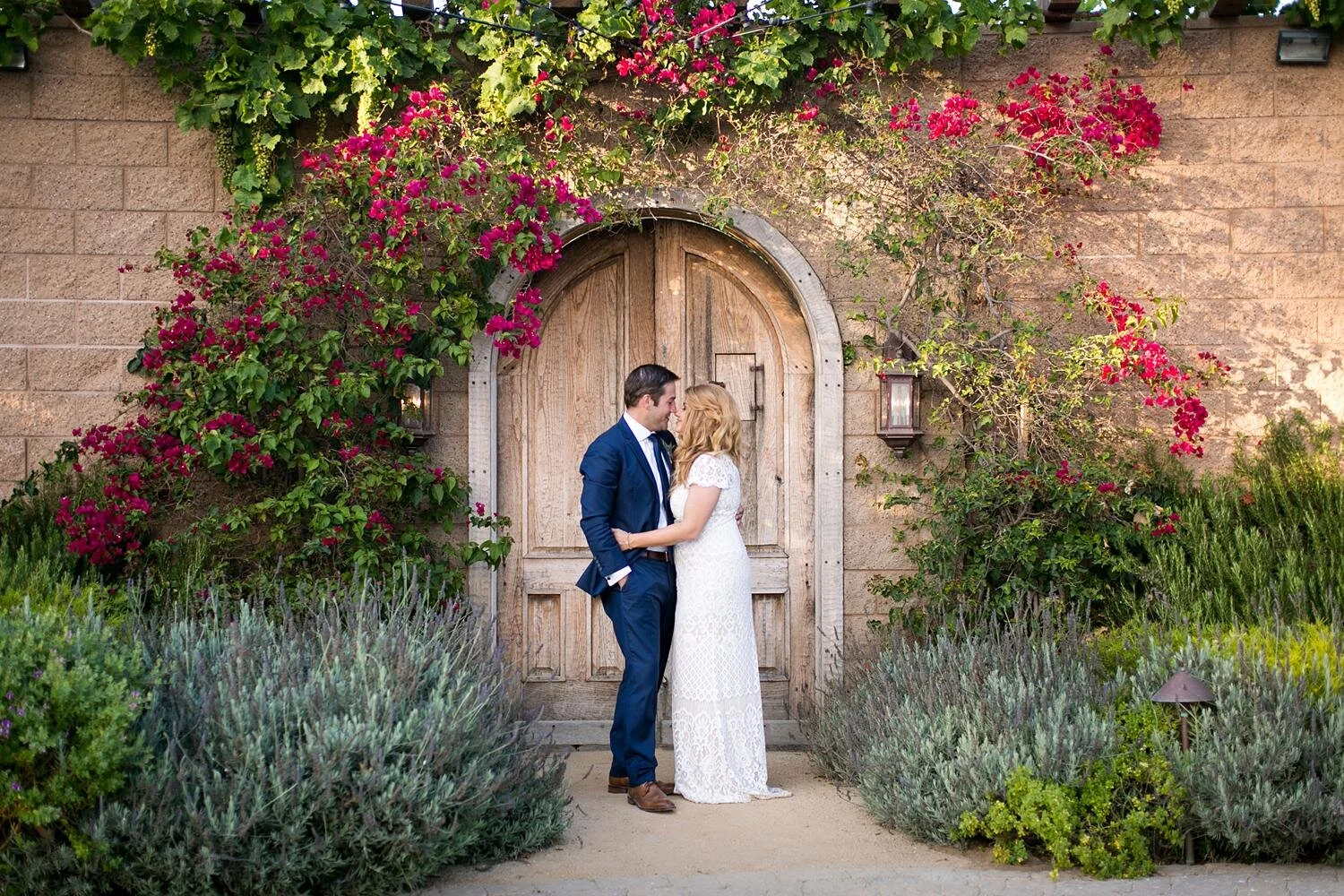 Wedding portrait of bride and groom by wooden doors and bougainvillea at Catalina View Gardens