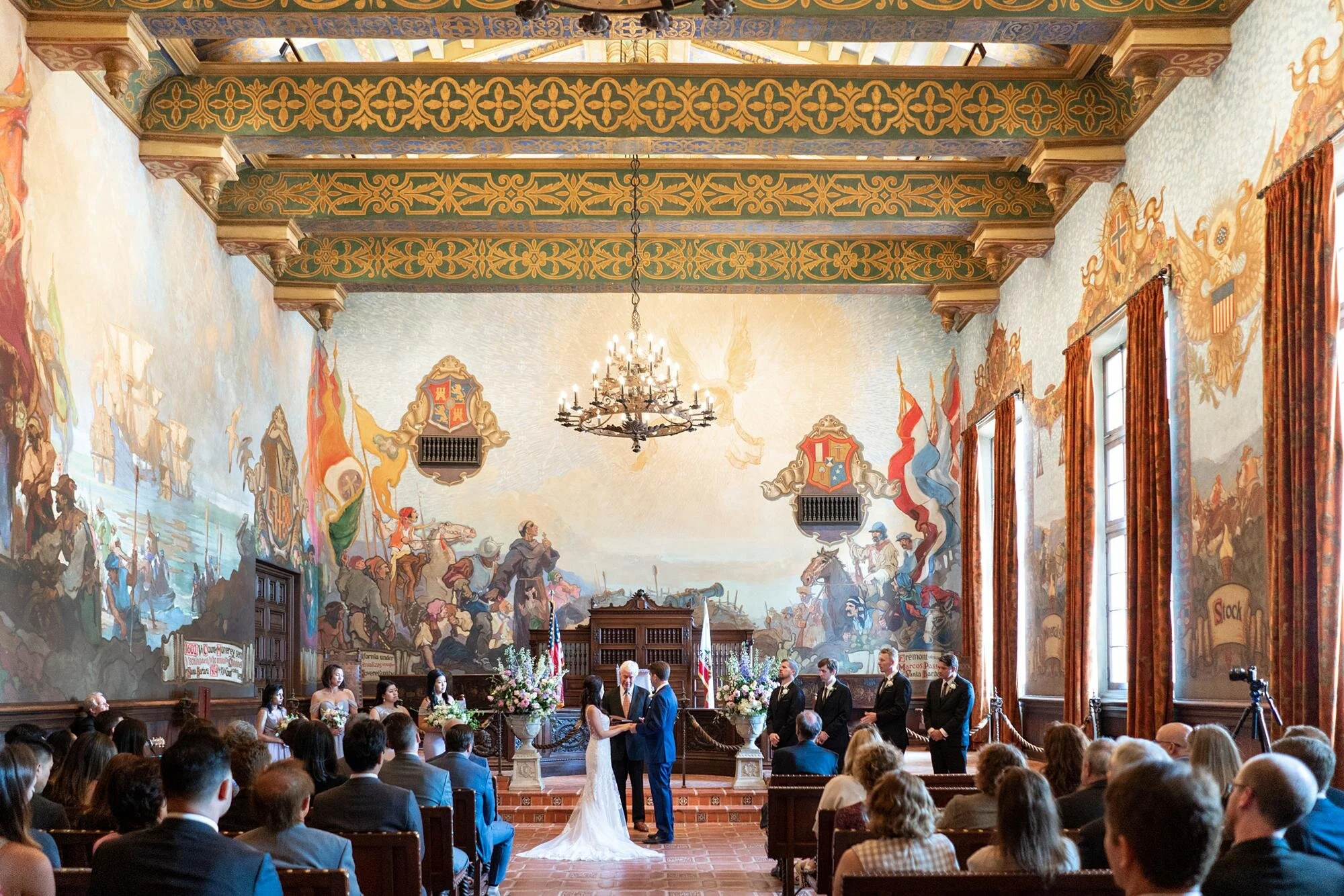 Wedding ceremony in the Mural Room at the Santa Barbara Courthouse as guests watch vows