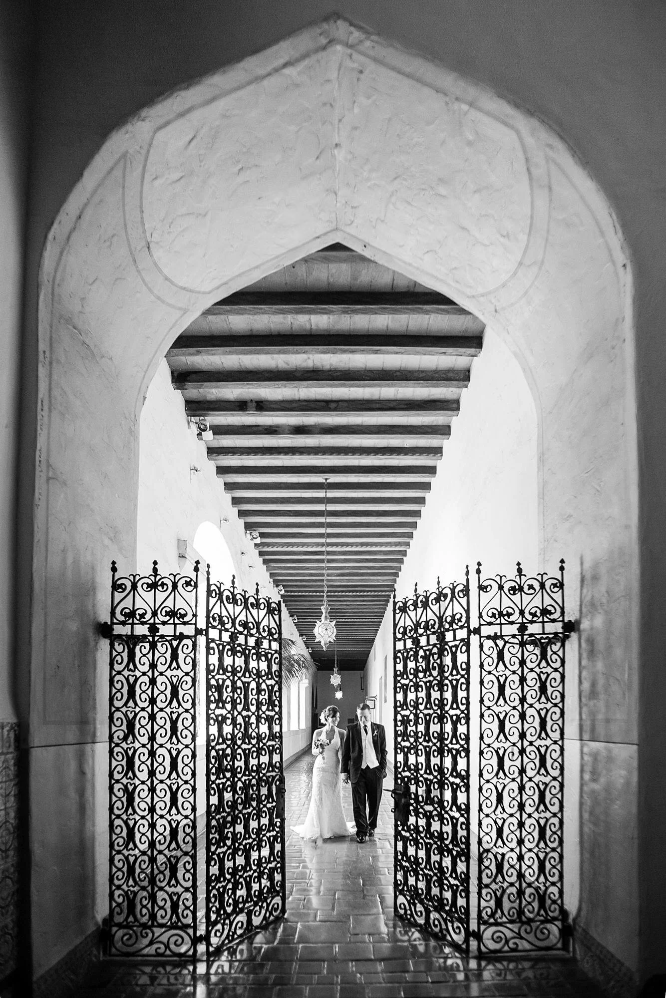 Wedding portrait of bride and groom walking between decorative iron gate at the Santa Barbara Courthouse