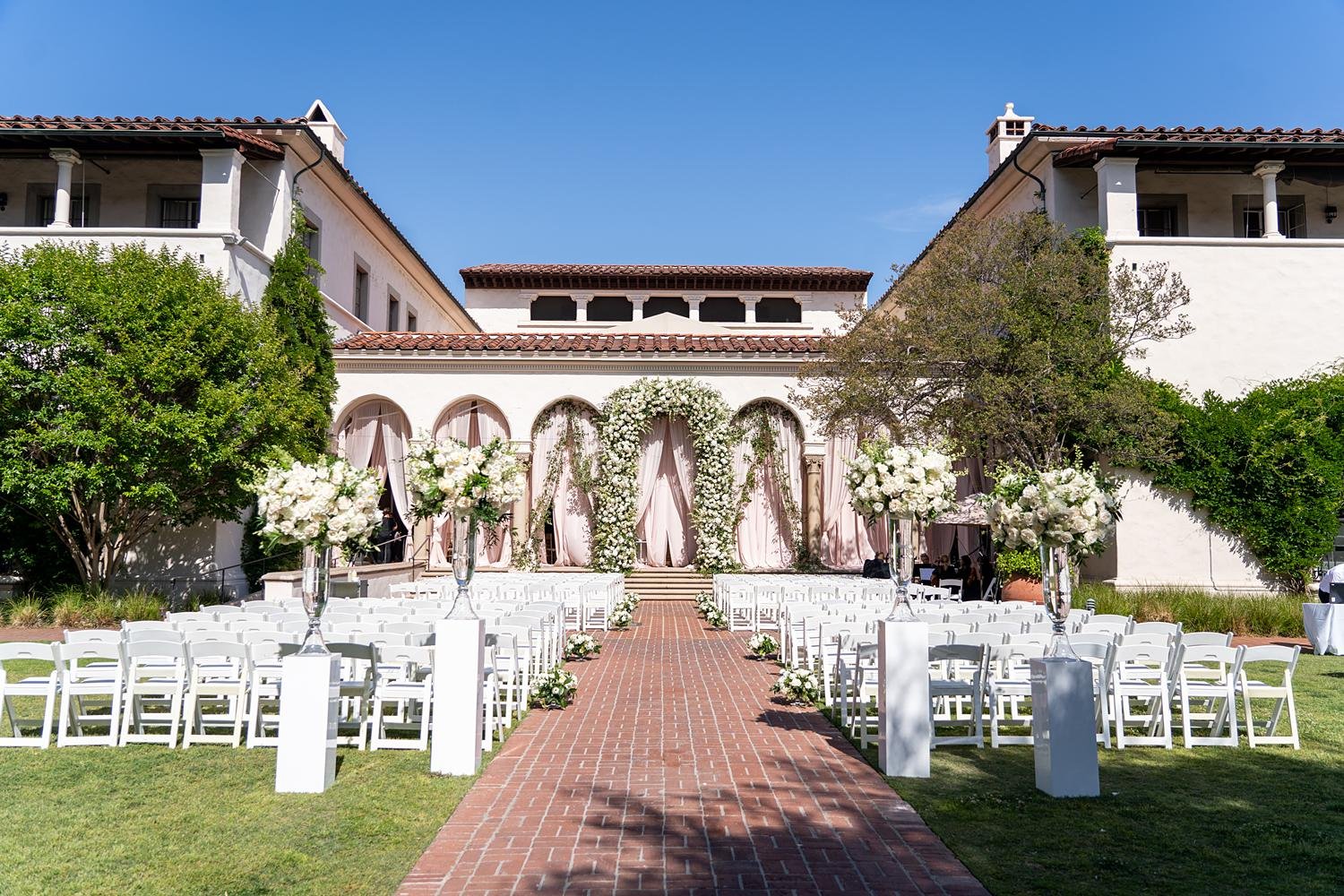 Wedding ceremony facing pink draped arches and white rose floral arch in the Courtyard at Athenaeum at Caltech