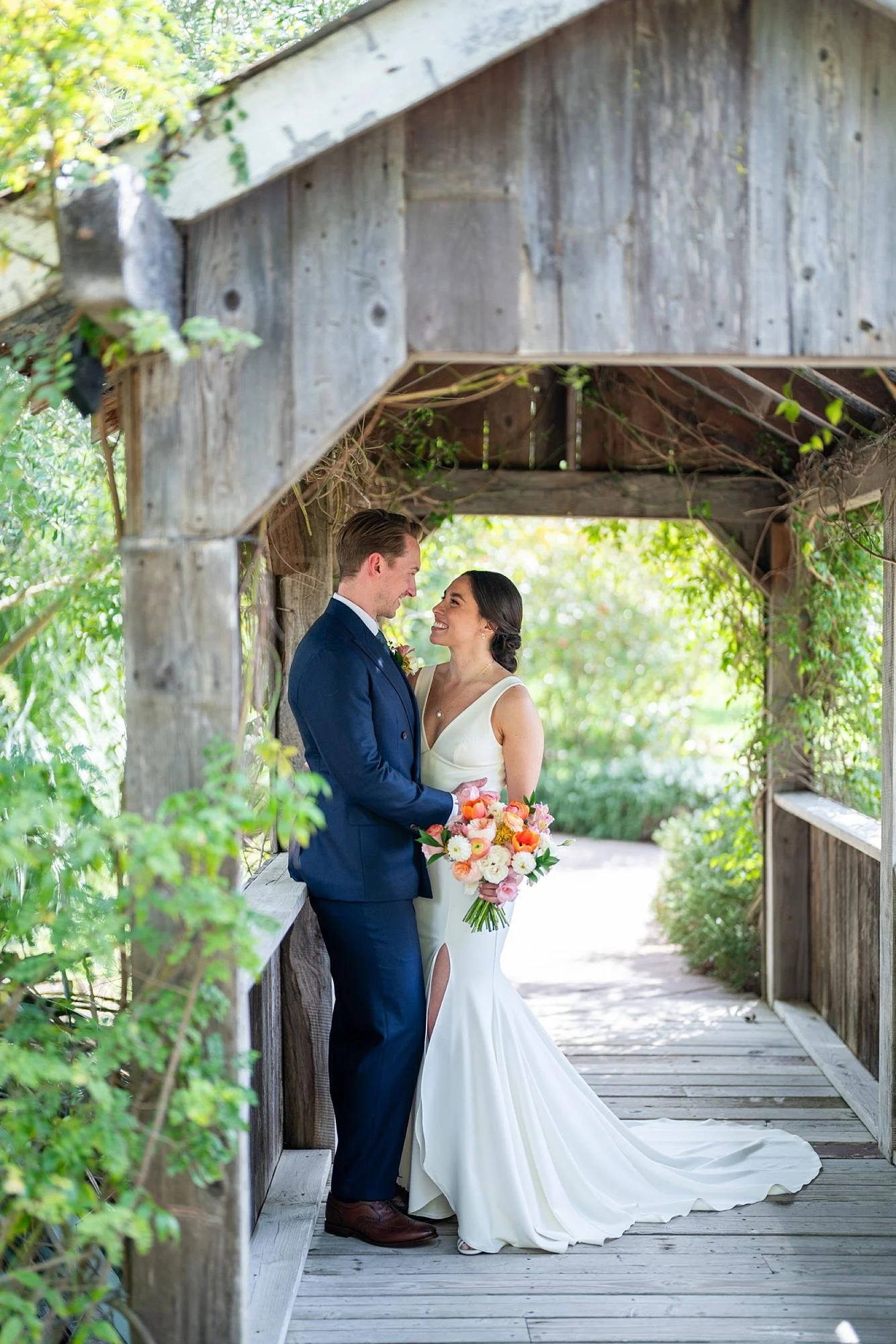 Wedding portrait of bride and groom looking at each other beneath the covered bridge at La Arboleda