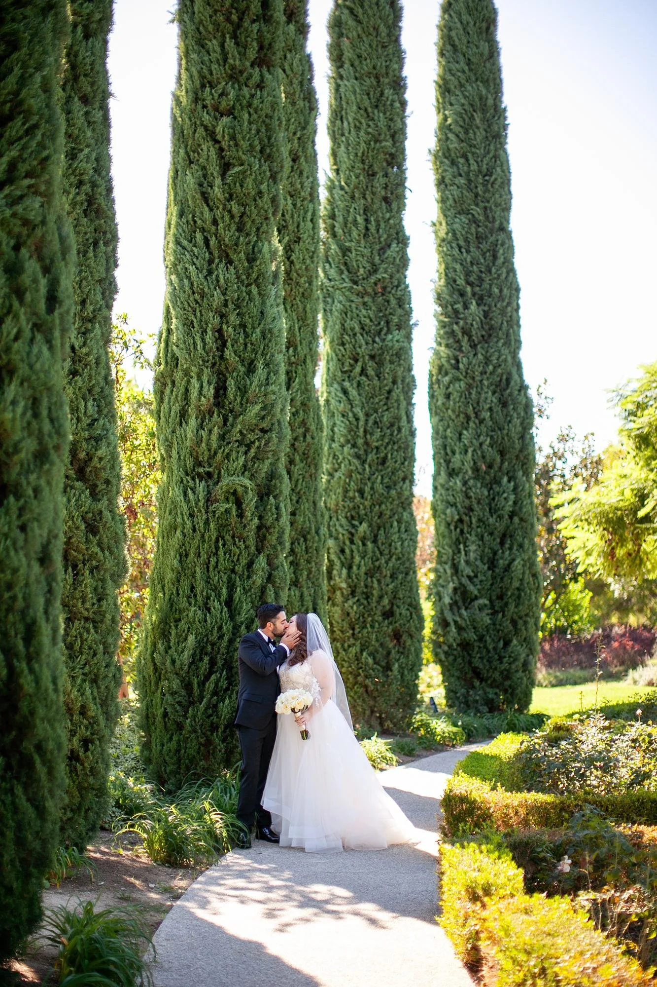 Wedding portrait at the Four Seasons Westlake with a kiss along a cypress-lined garden path