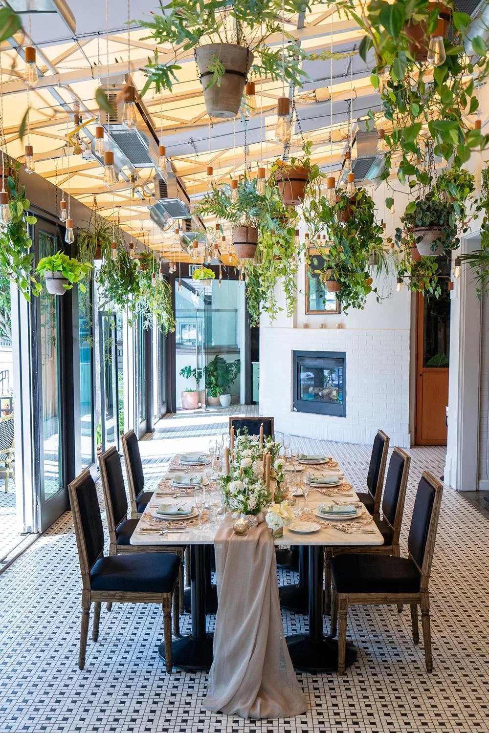 Wide view of Fig Restaurant wedding reception tables decorated with fabric, florals, and hanging plants
