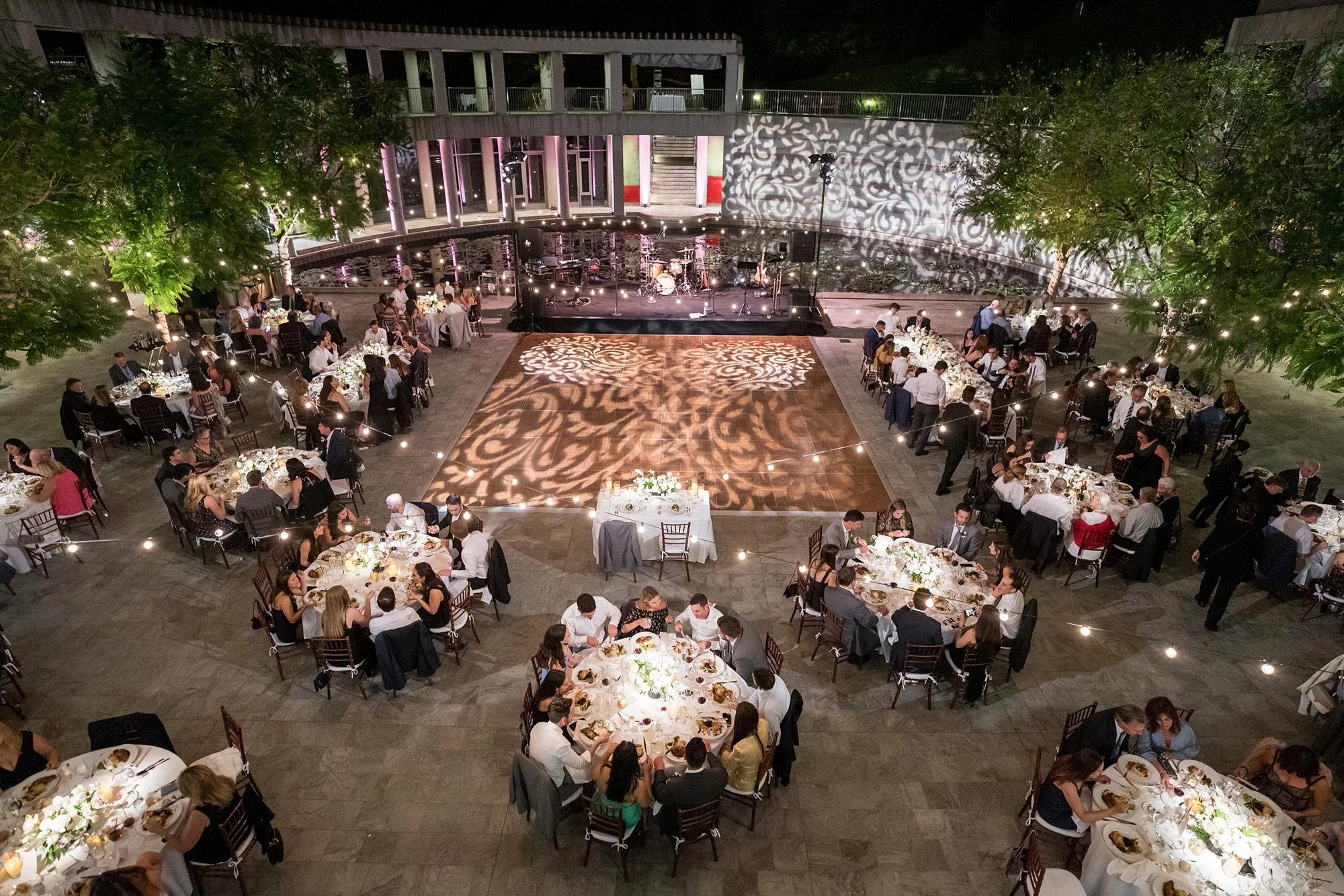 Guests enjoying dinner during an evening wedding reception in the Taper Courtyard at the Skirball Cultural Center
