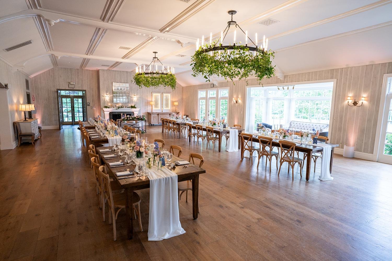 Wedding reception in the Lodge at Malibou Lake Ballroom with chandeliers draped in greenery above tables