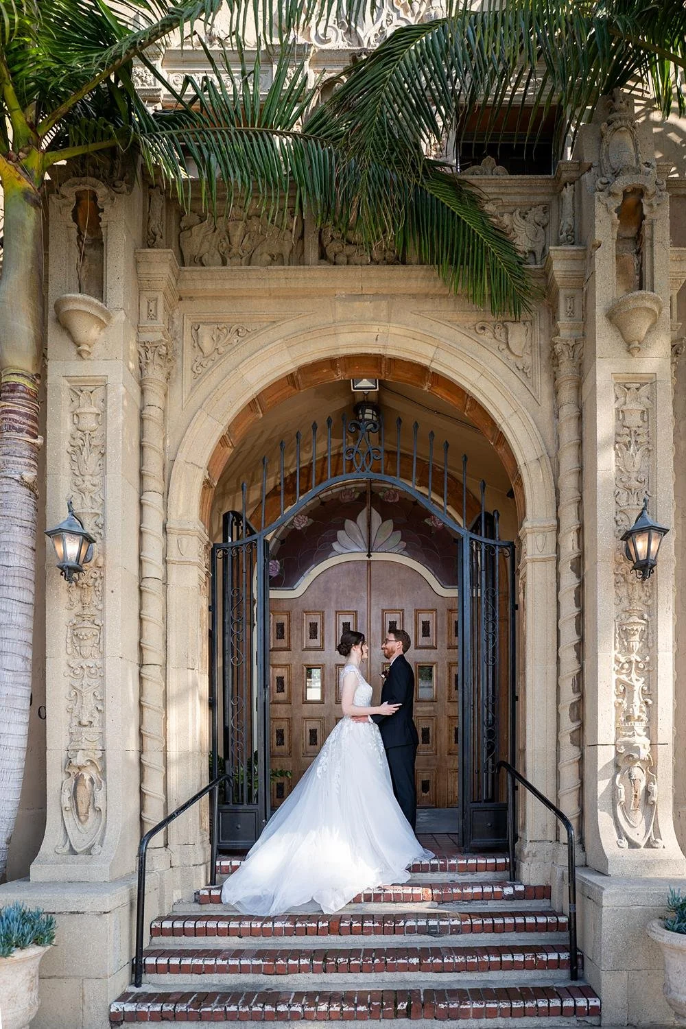 Wedding portraits of bride and groom on entrance stairs beneath arch and palms at the Ebell of Long Beach
