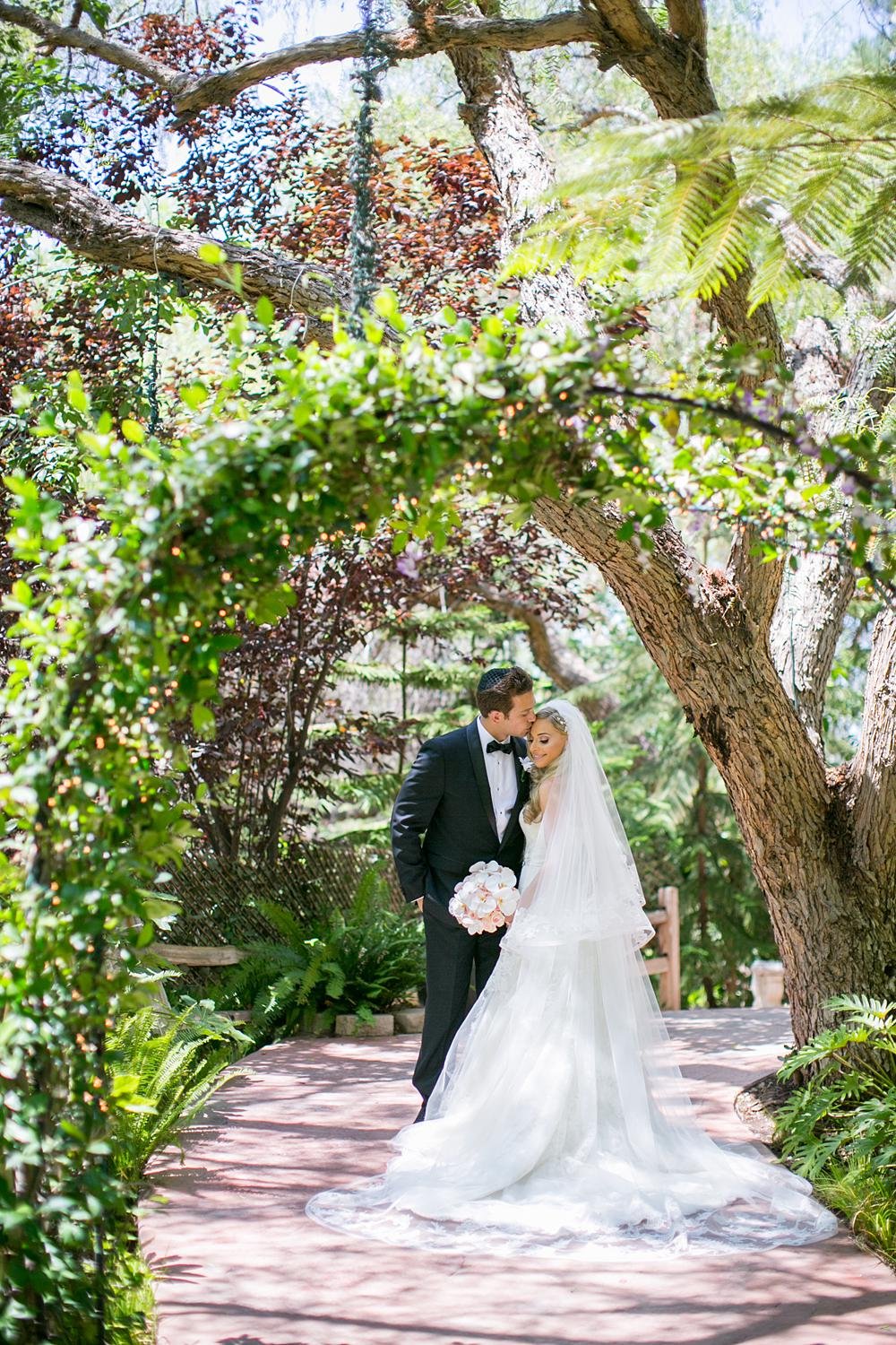 Wedding portraits of groom kissing bride under ivy arch at The Vineyards Simi Valley